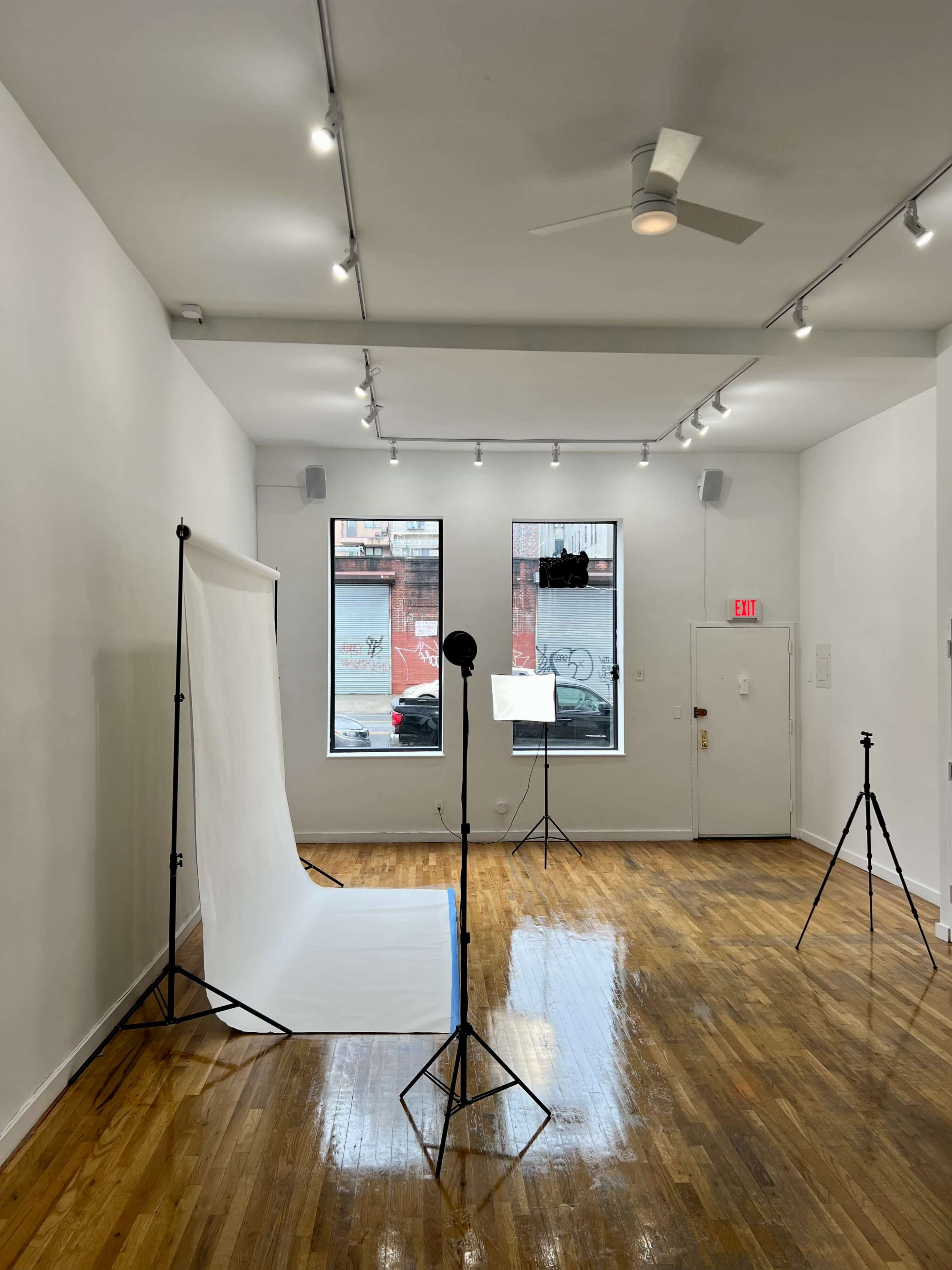 A photography studio featuring a white backdrop, lighting equipment, and large windows.