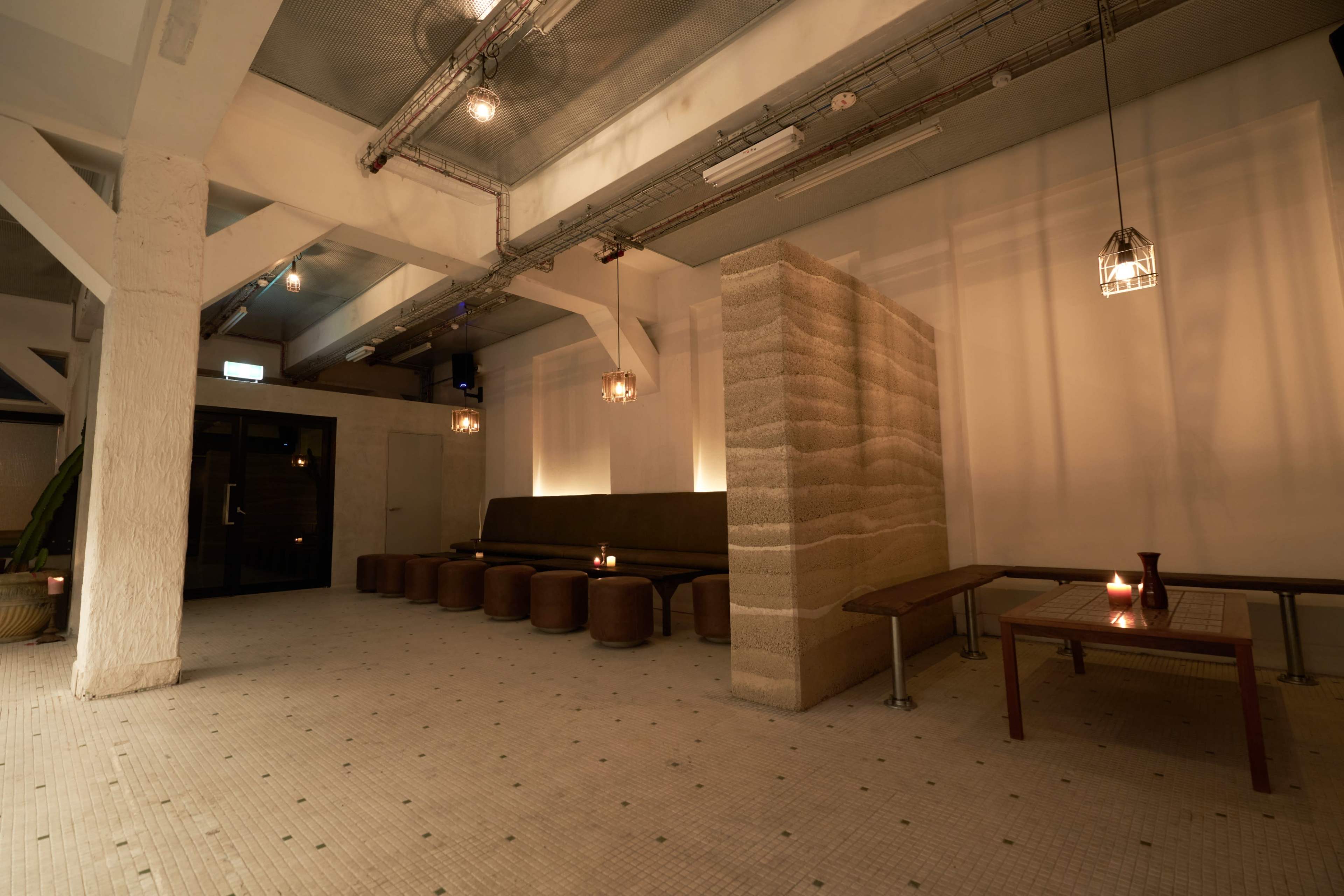 The image shows a spacious indoor area with a low seating arrangement, wooden tables, and soft lighting.