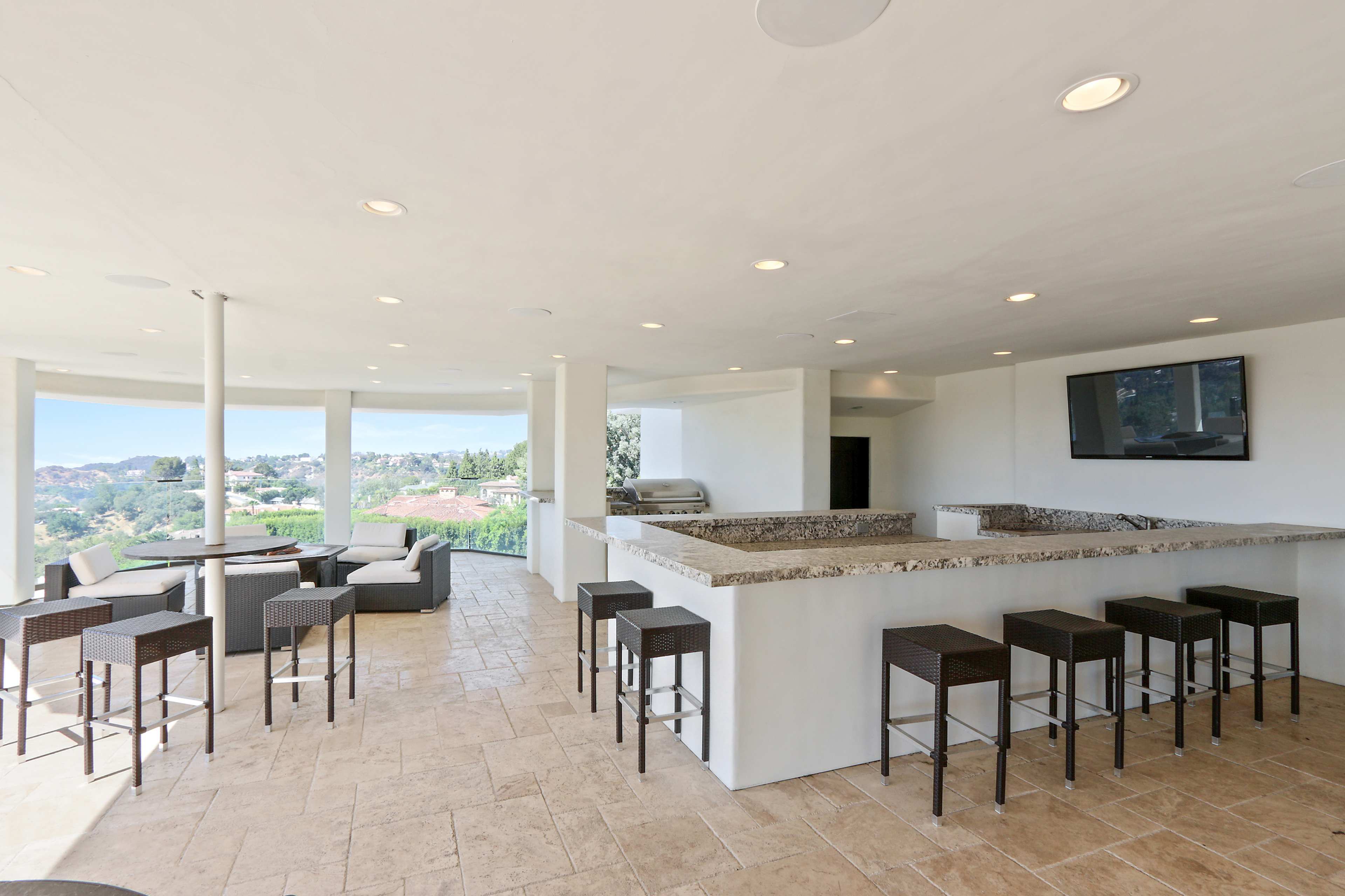 A modern outdoor bar area with a granite countertop, seating for eight, and a scenic view beyond.