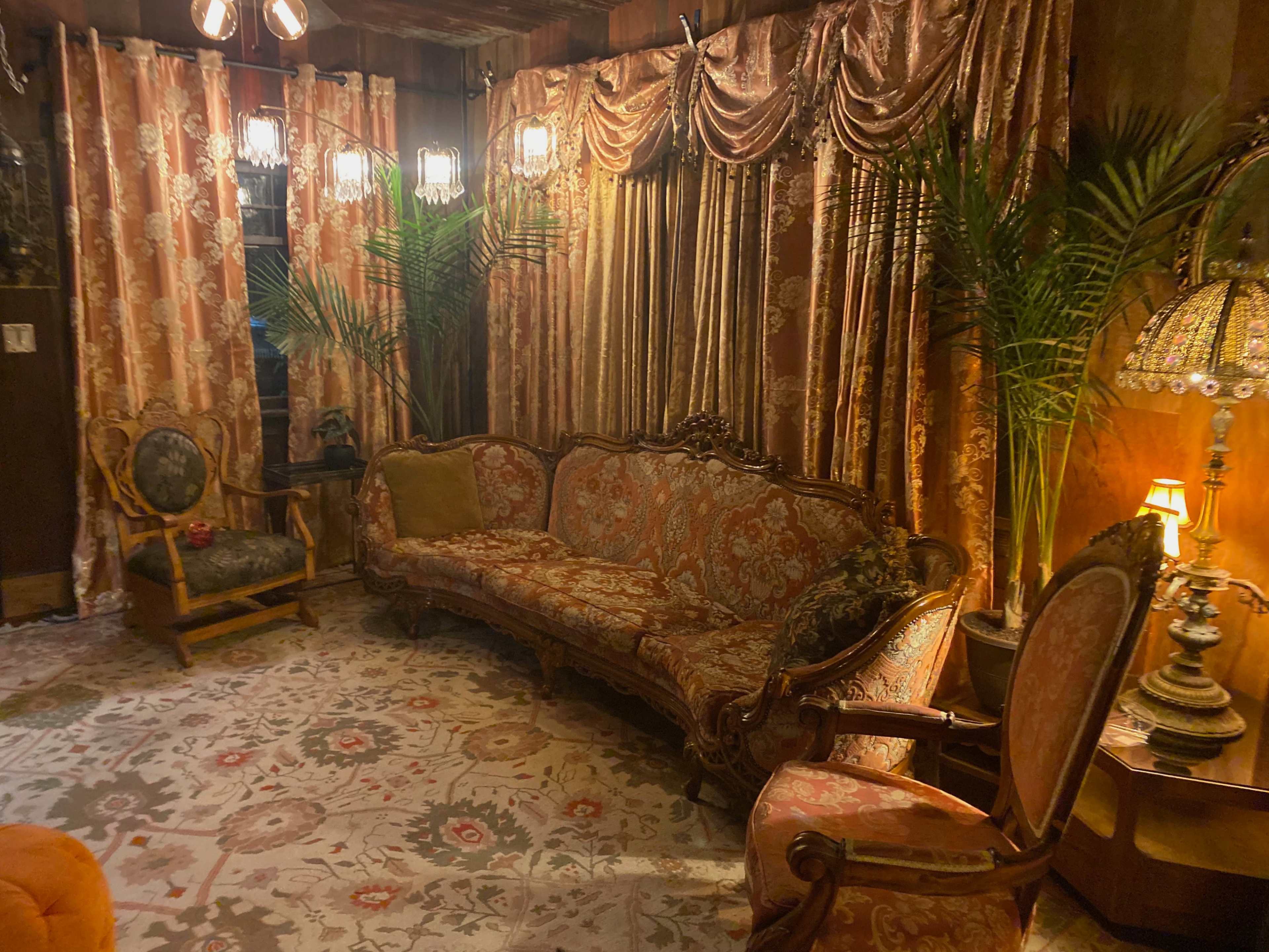 A vintage living room with ornate furniture, patterned curtains, and decorative lamps.