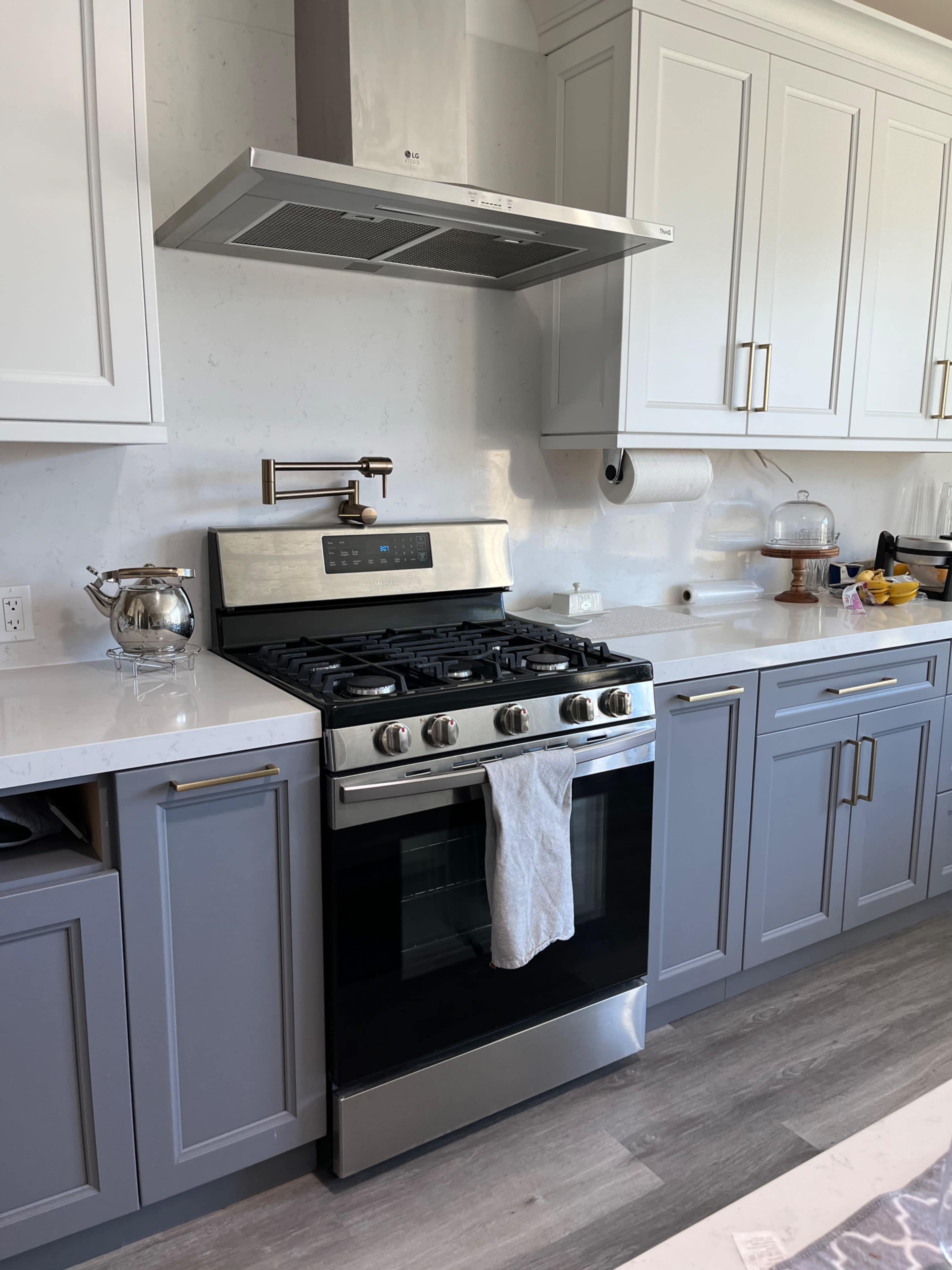 A modern kitchen features a stainless steel gas stove with a range hood, gray cabinets, and a white countertop.