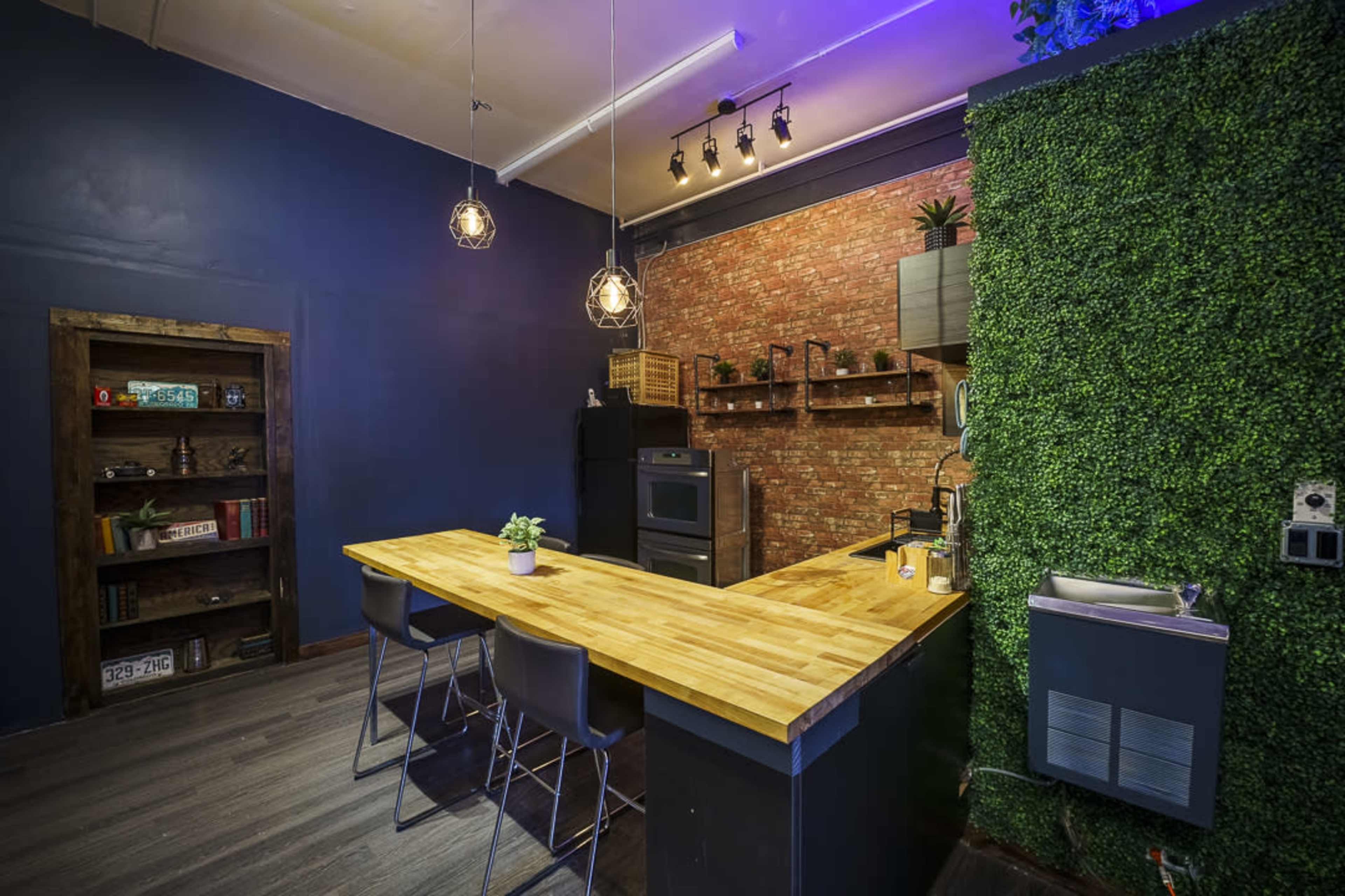 A modern kitchen with a wooden island, black bar stools, a brick accent wall, and greenery on one side.