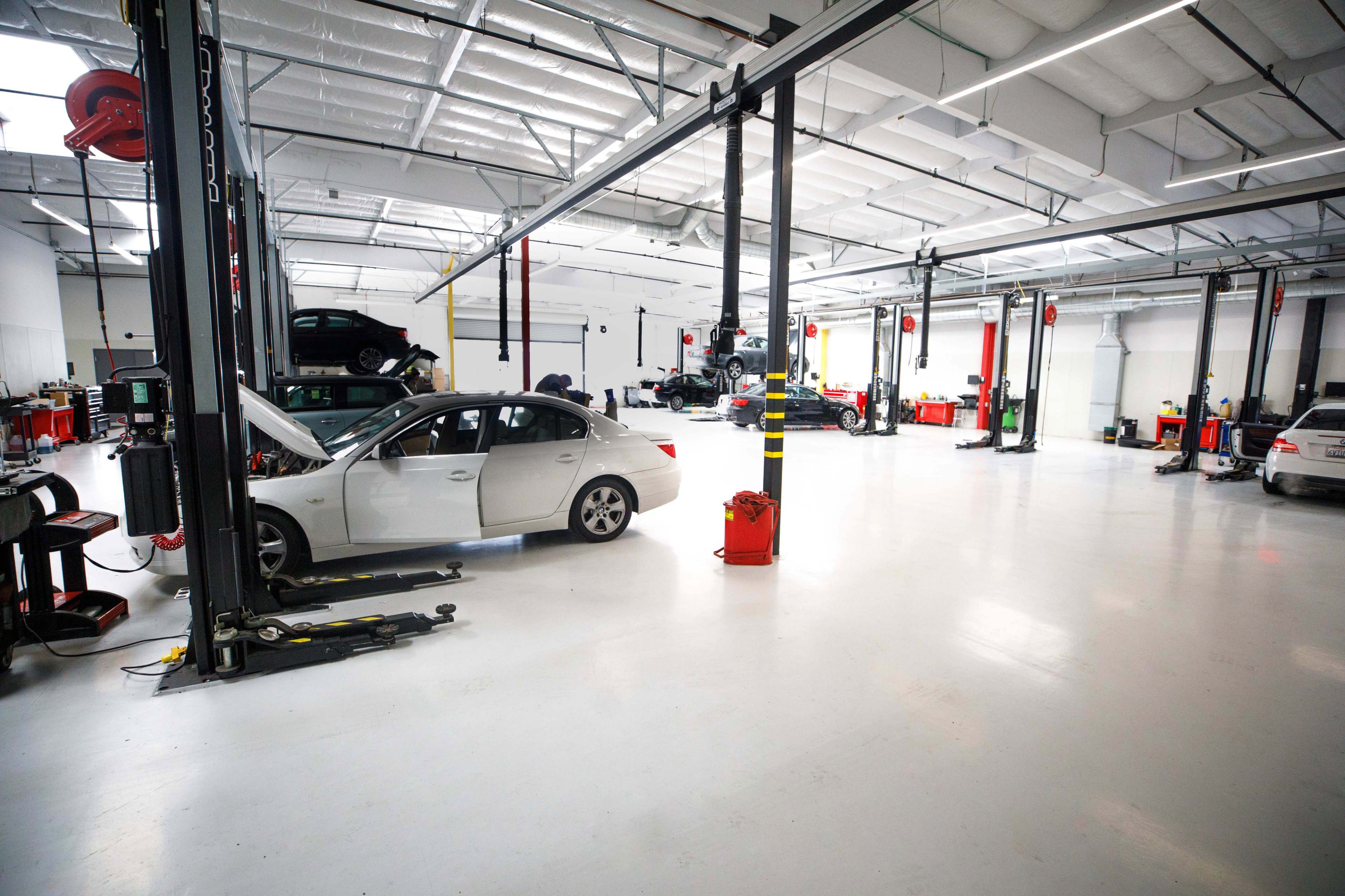 A spacious automotive repair shop with several cars on raised lifts and various tools and equipment organized around the area.