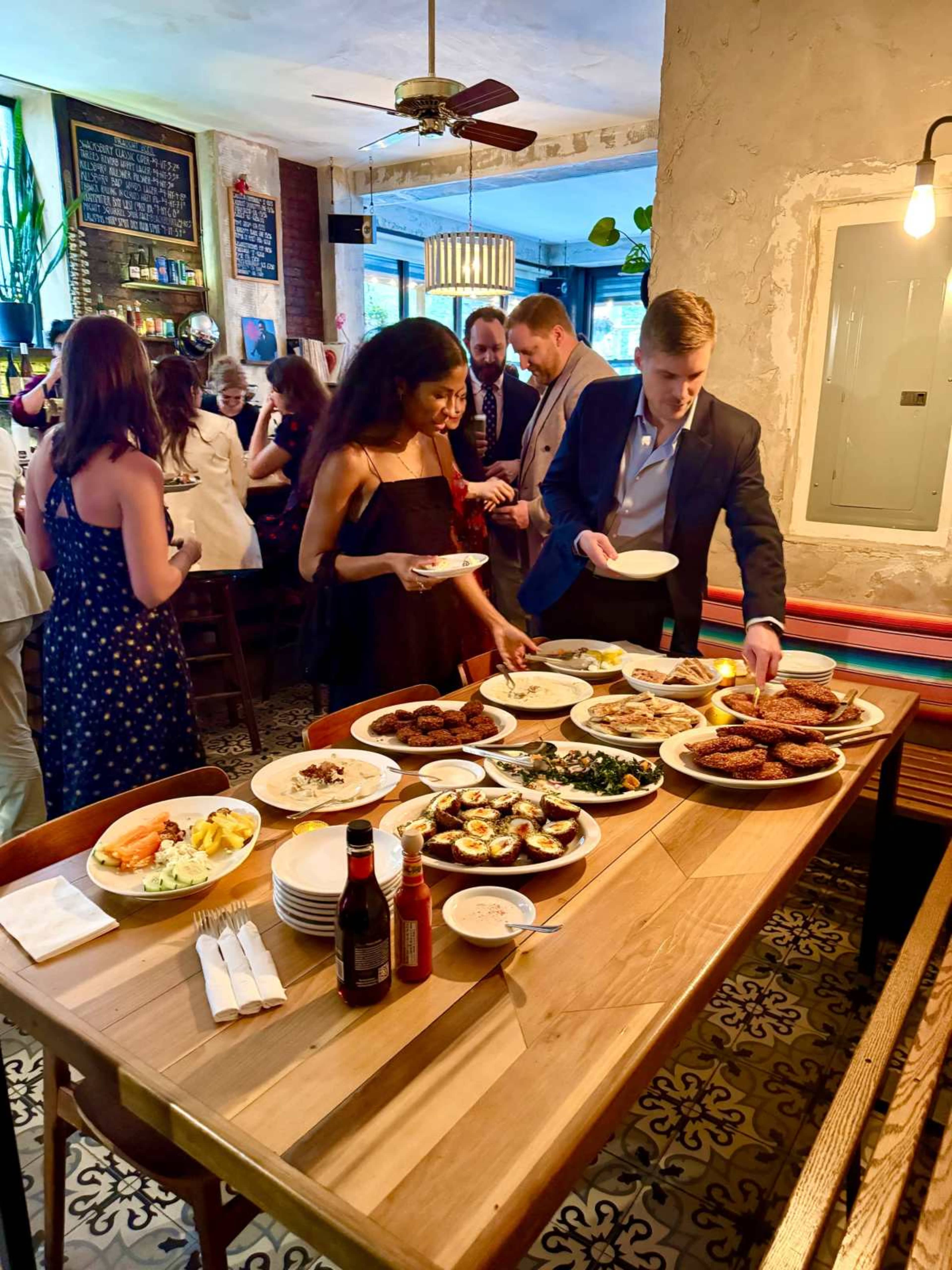 A diverse group of people gathers around a table filled with various dishes and appetizers in a lively dining setting.