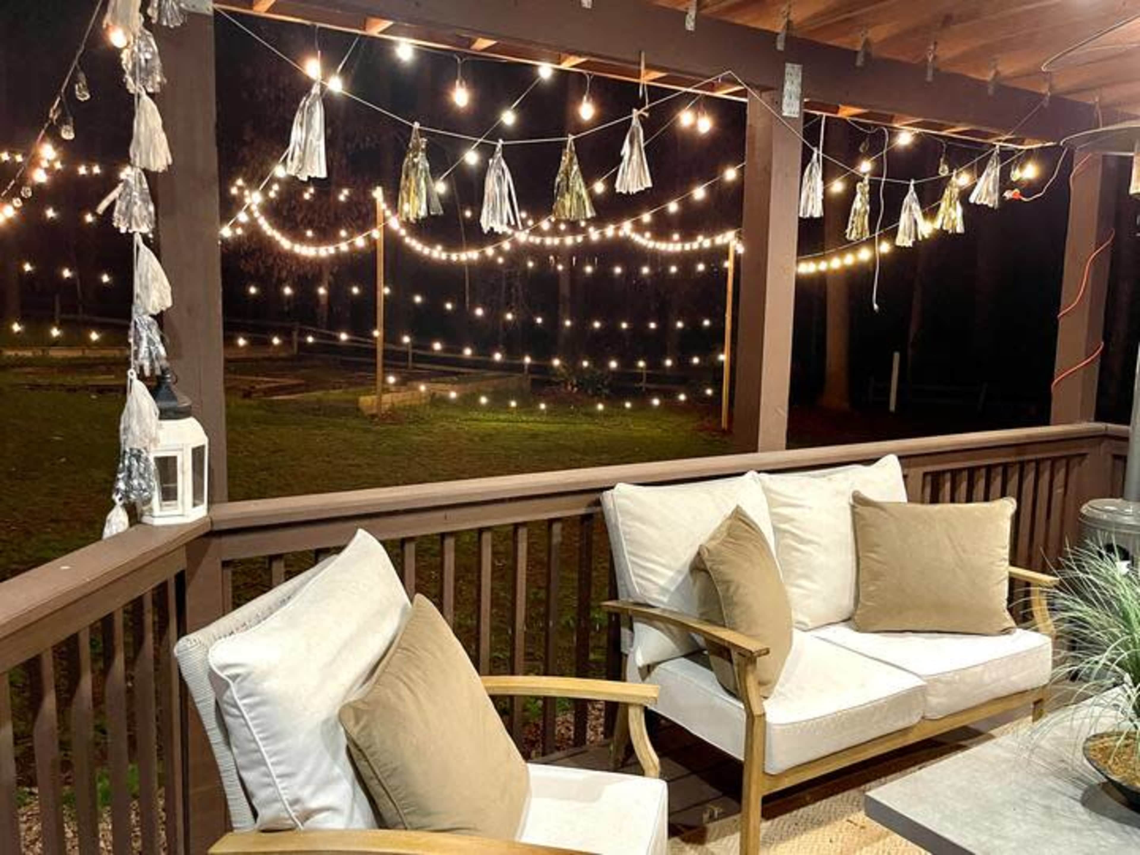 A cozy outdoor seating area features string lights and decorative tassels hanging above a sofa on a deck.