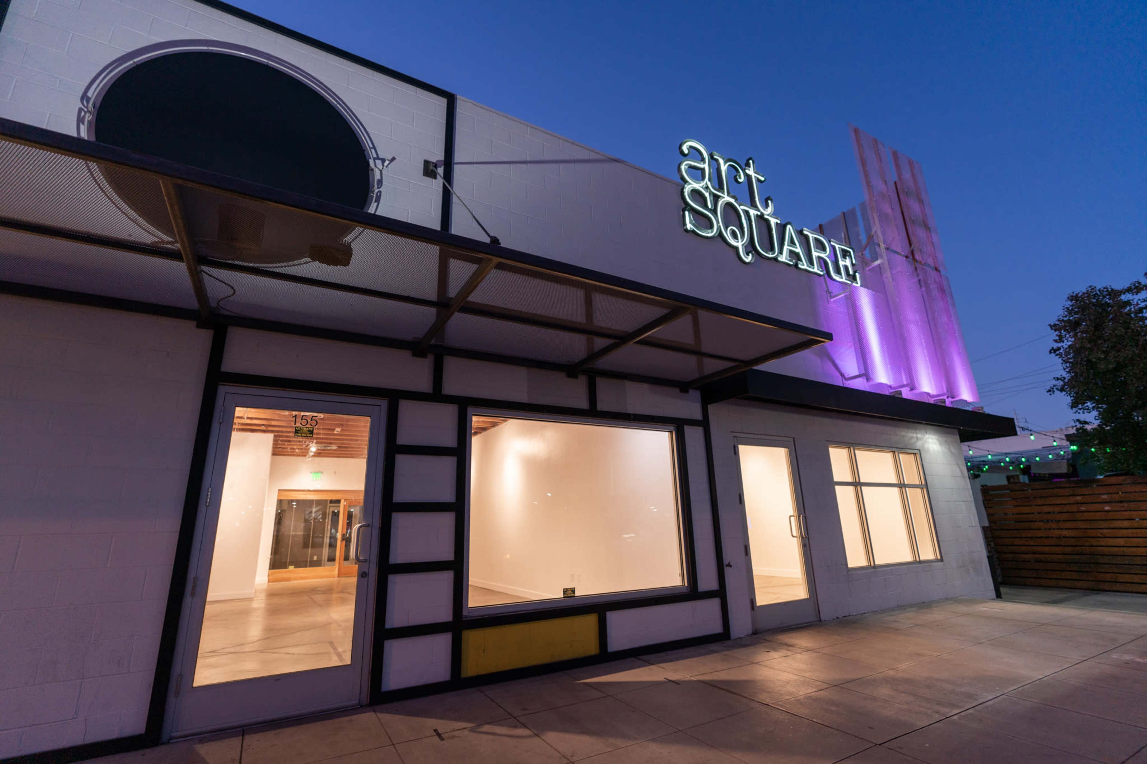 The exterior of a building named "art SQUARE" with large windows and a colorful lit sign during twilight.