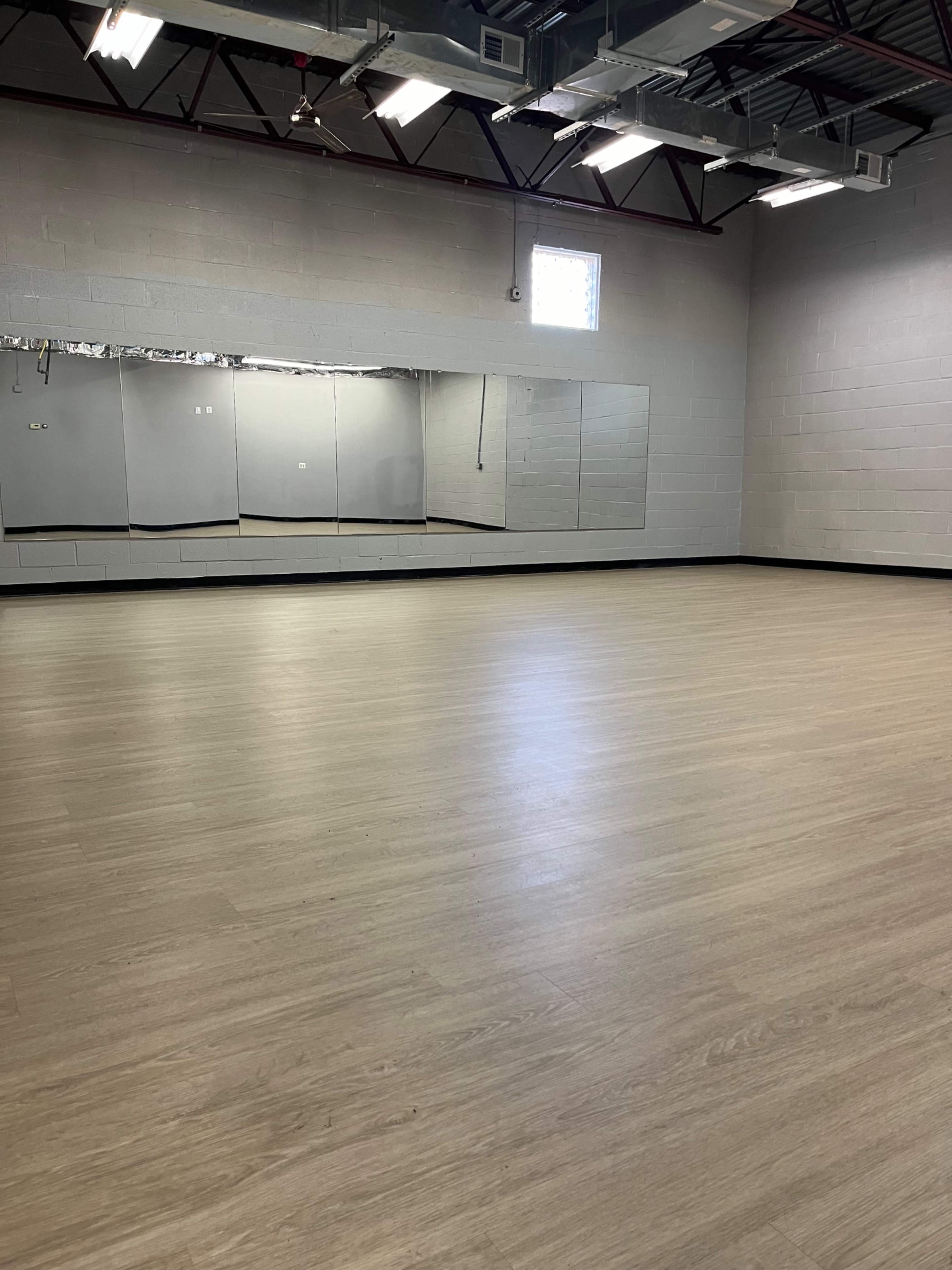 The image shows an empty dance studio with a large mirror along one wall and wooden flooring.