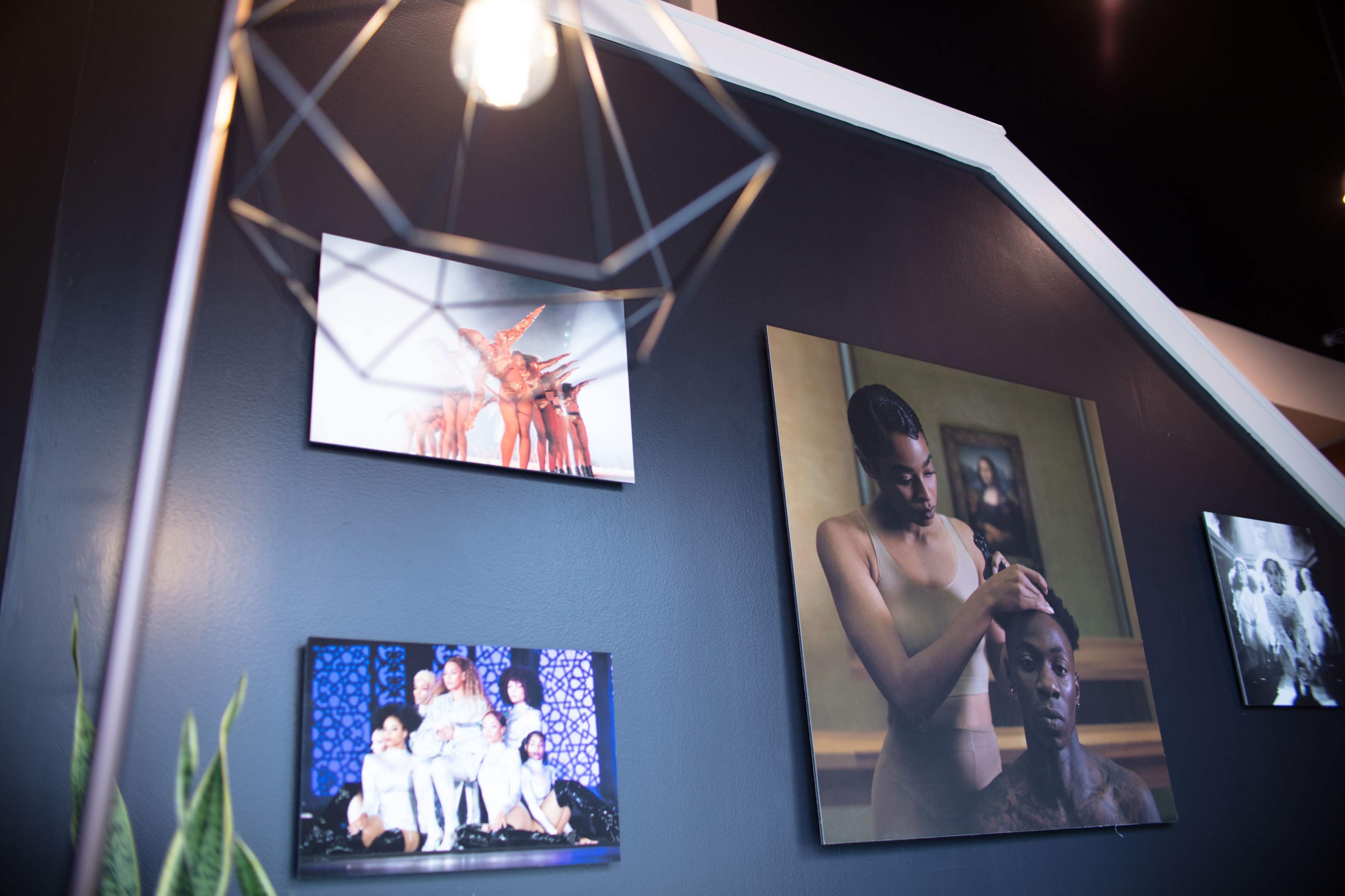 A black wall adorned with various framed photographs and a geometric pendant light hanging above.