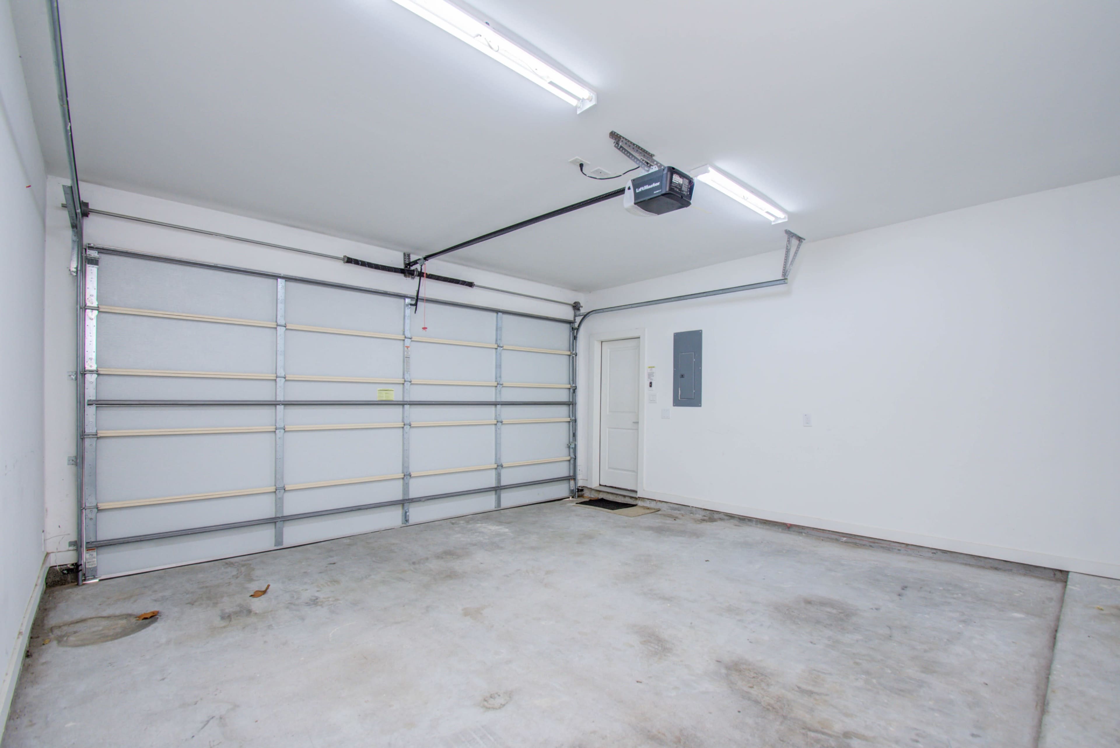 An empty garage with a concrete floor, a large sectional door, and a side door leading outside.