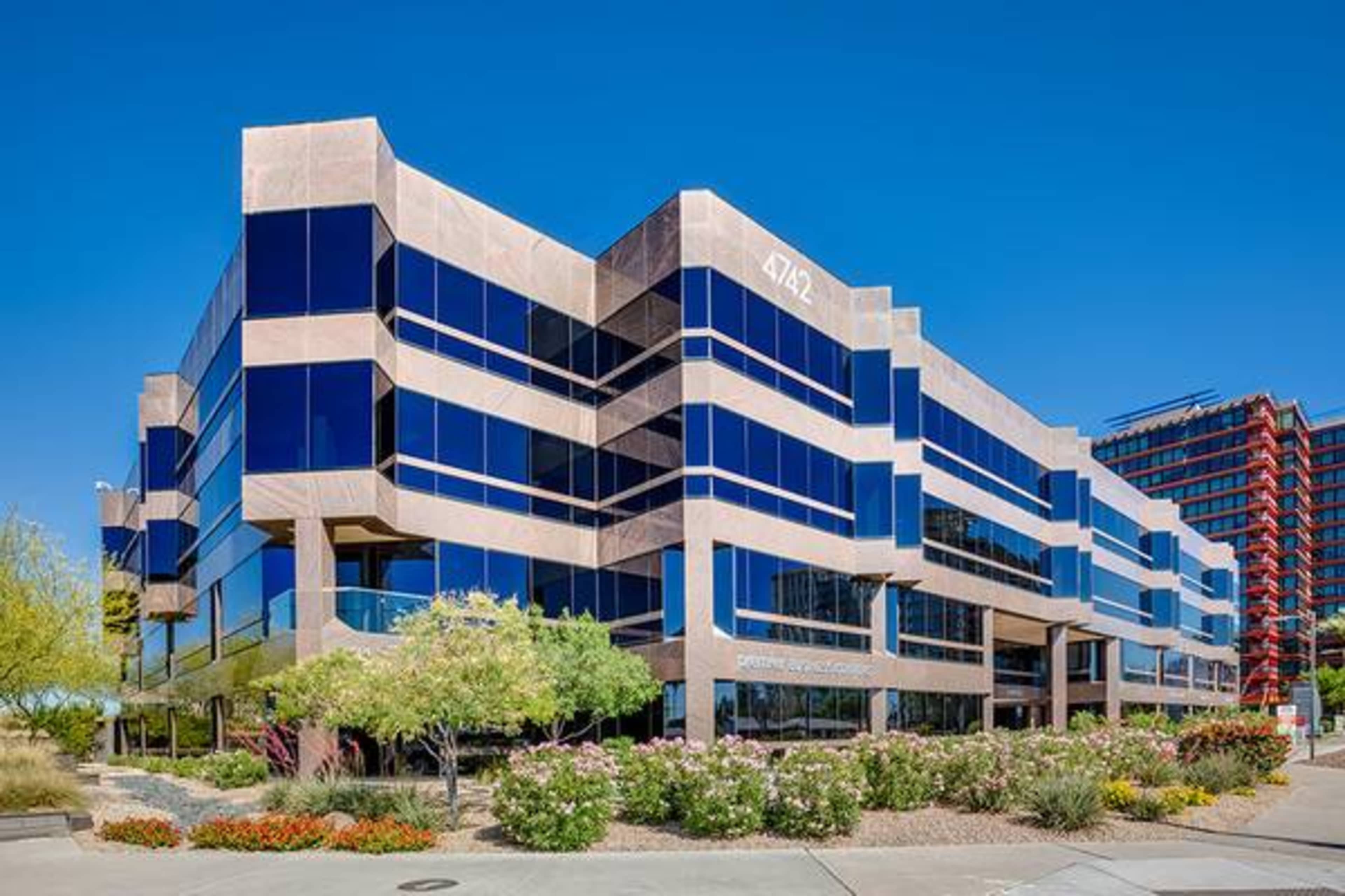 A modern multi-story office building with large glass windows and landscaped greenery in the foreground.