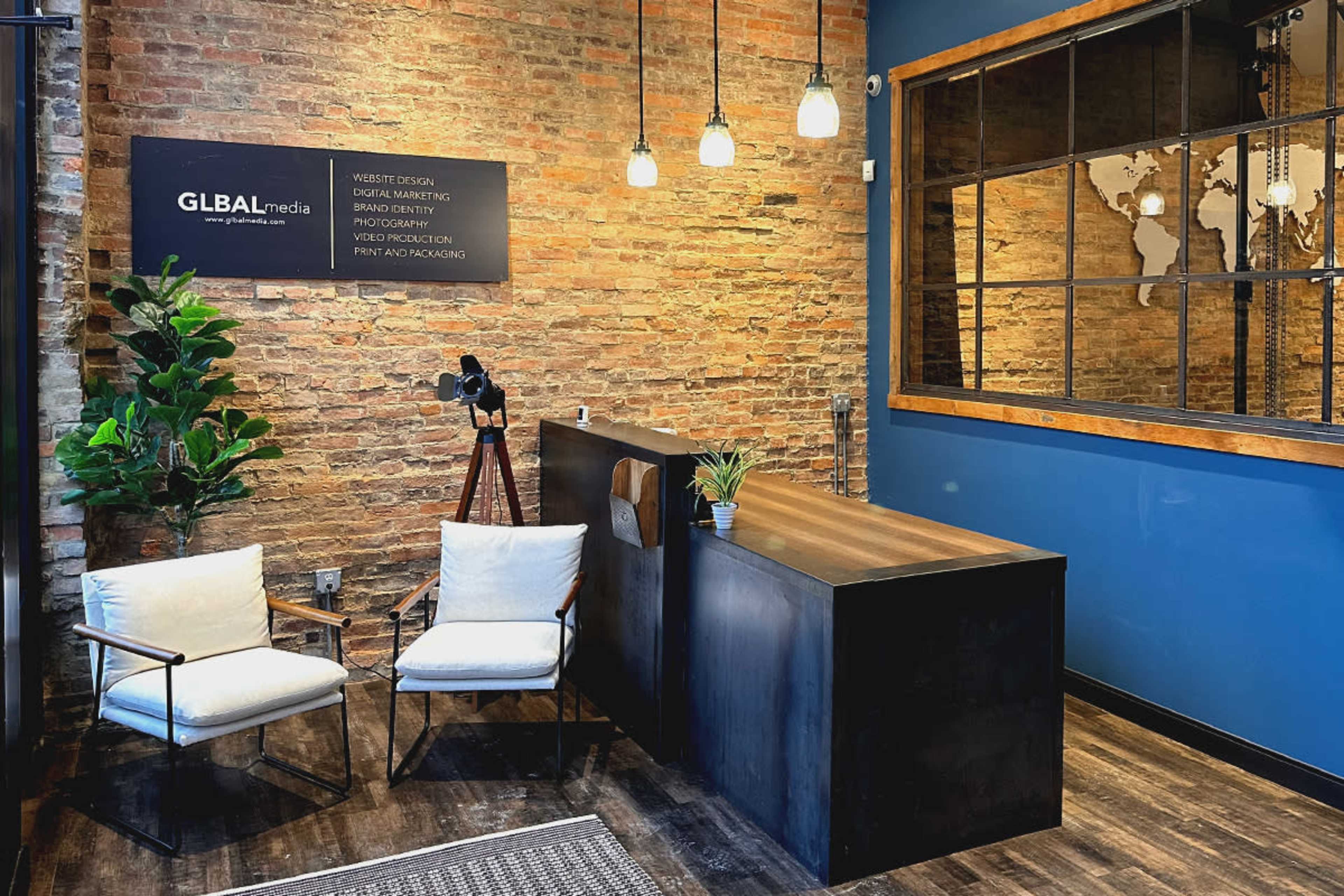A reception area with a wooden desk, two chairs, a plant, and a wall featuring a company sign and a world map.