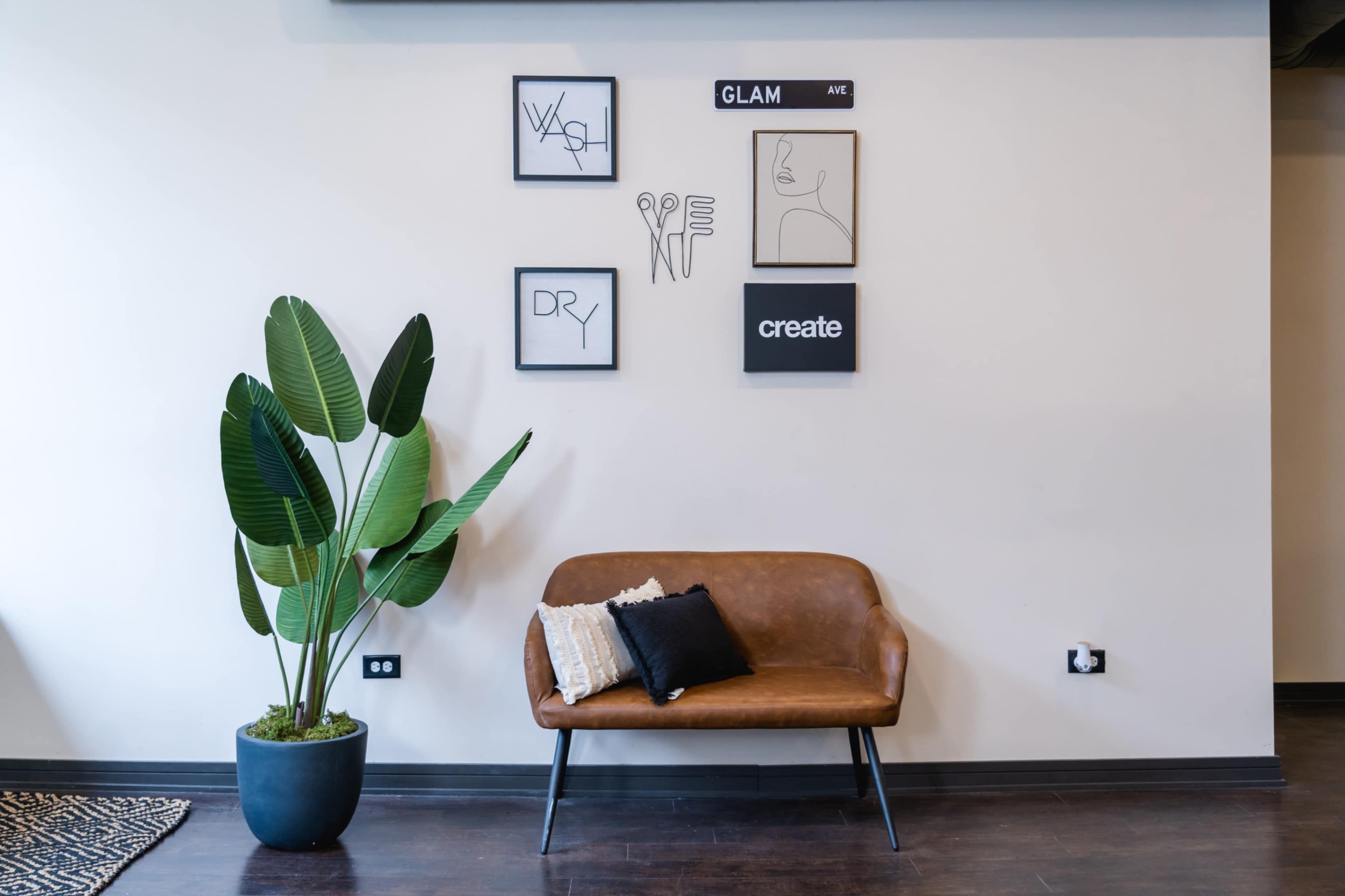 A cozy interior space featuring a brown leather sofa, a potted plant, and framed artworks on the wall.