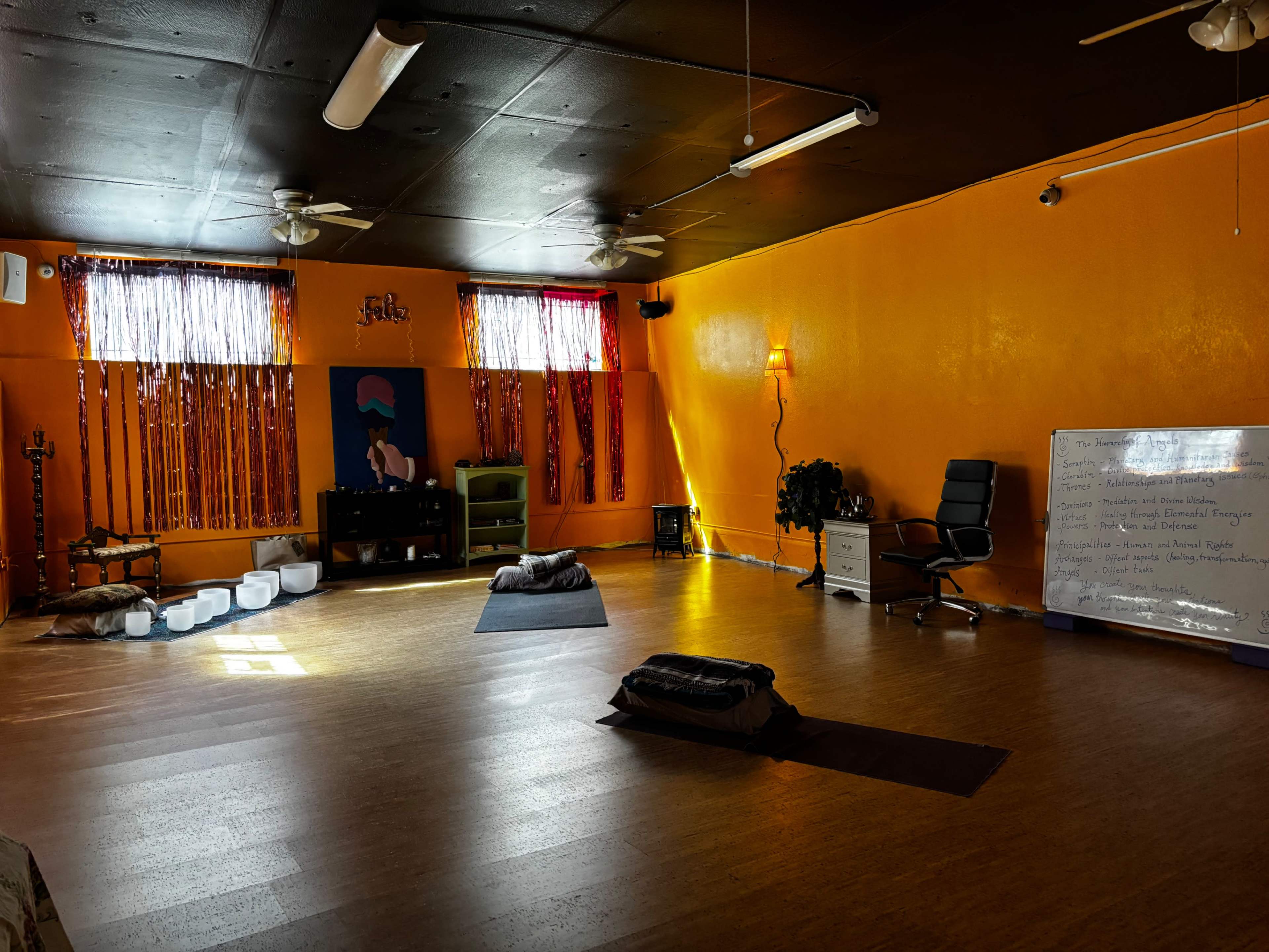 The image shows a yoga studio with orange walls, natural lighting, and various meditation cushions arranged on the wooden floor.