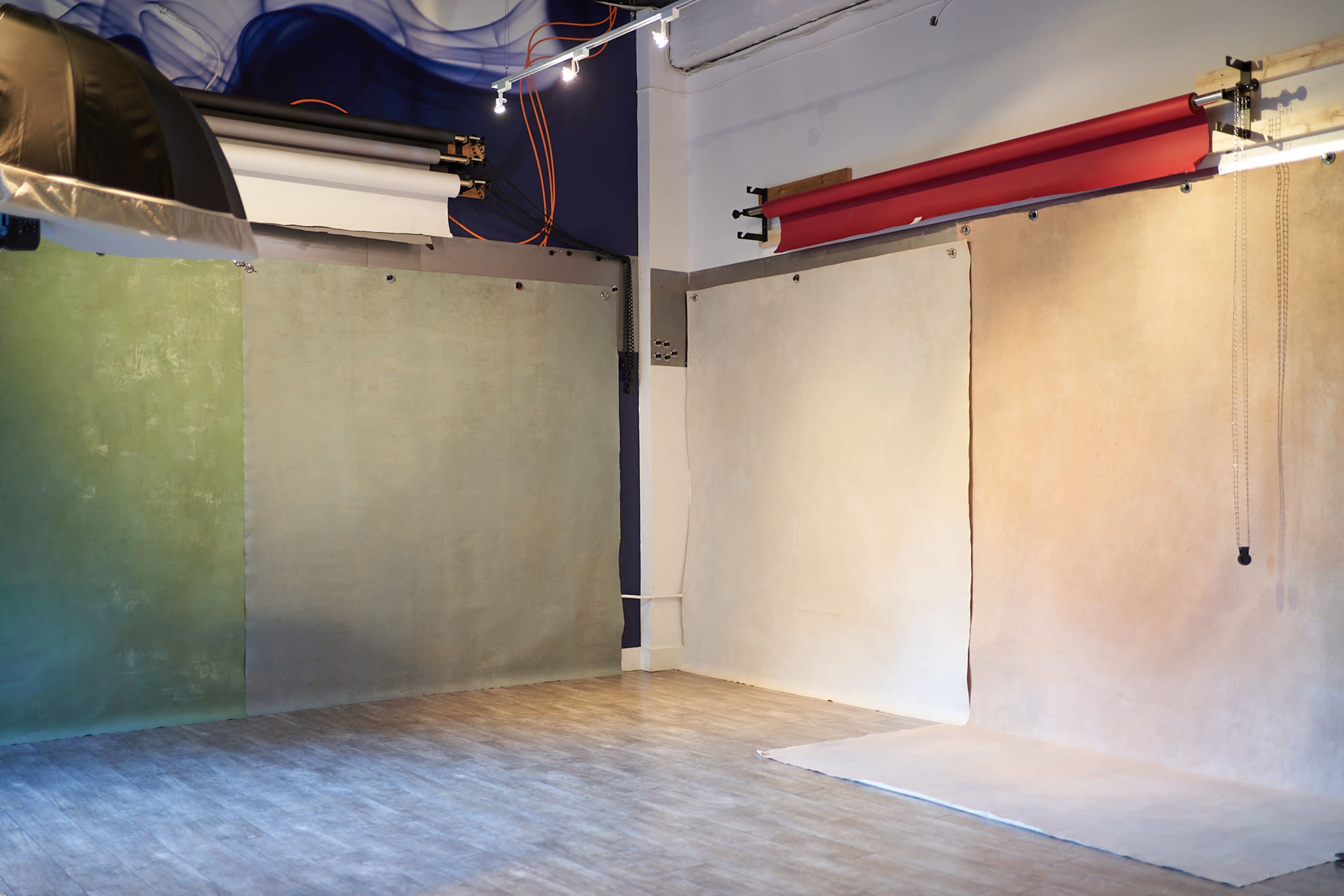 The image shows a photography studio with three large, colorful backdrops hung on the walls and a wooden floor.