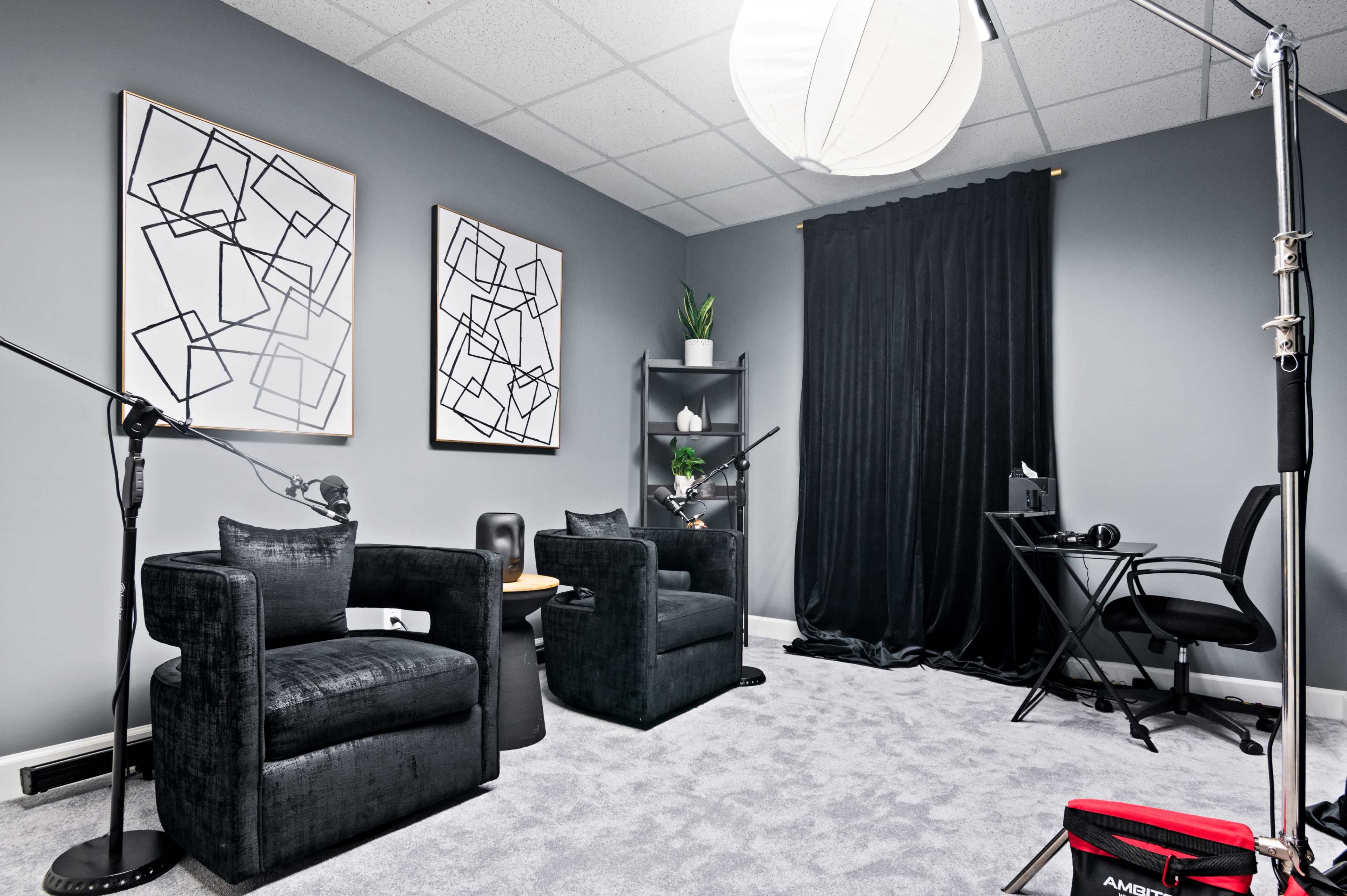 A modern interior space featuring two black armchairs, a table, a desk with a computer, and framed art on the walls.