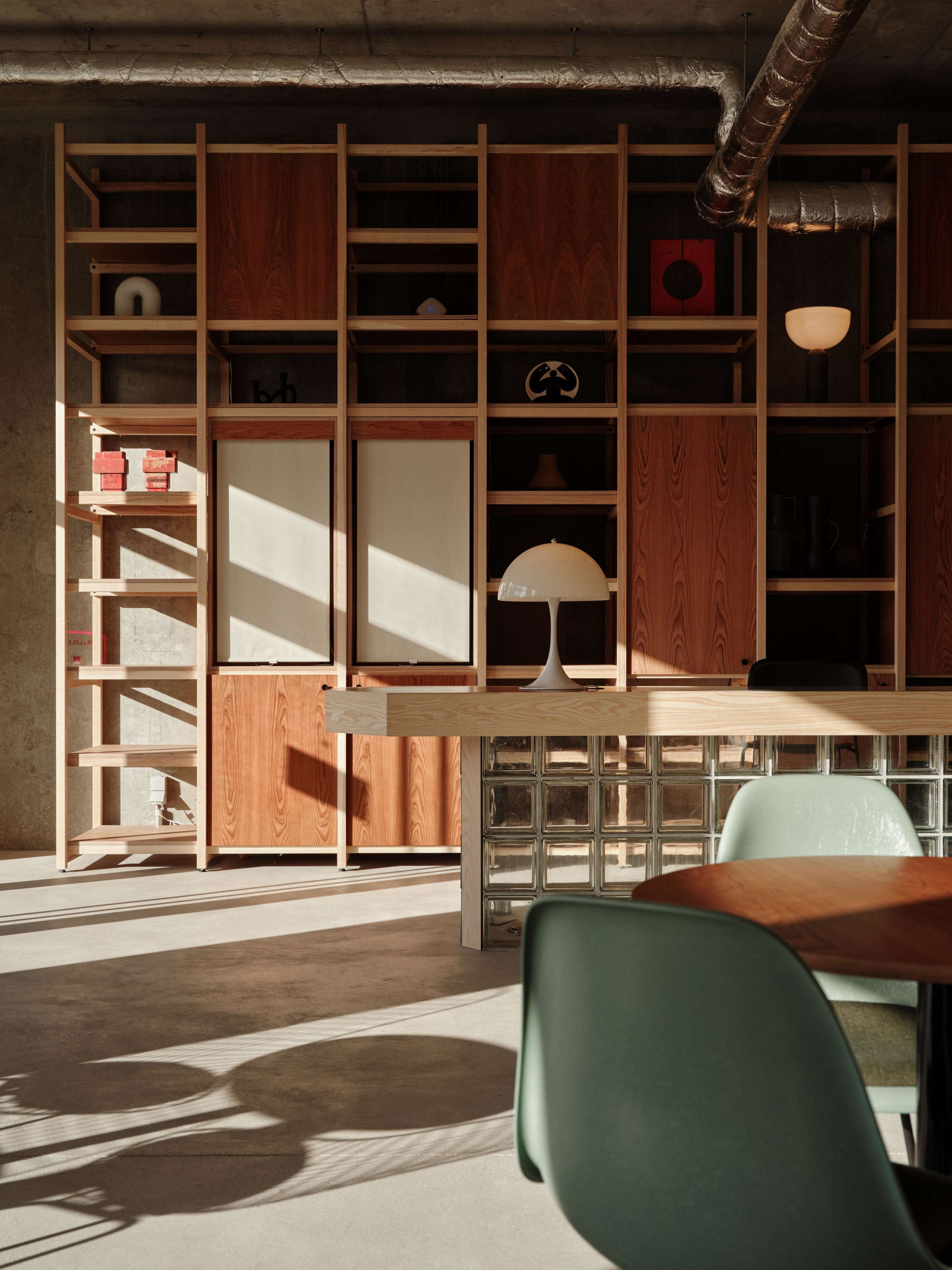The image shows a modern interior with wooden shelving, a glass block wall, and a lamp on a table, illuminated by sunlight.