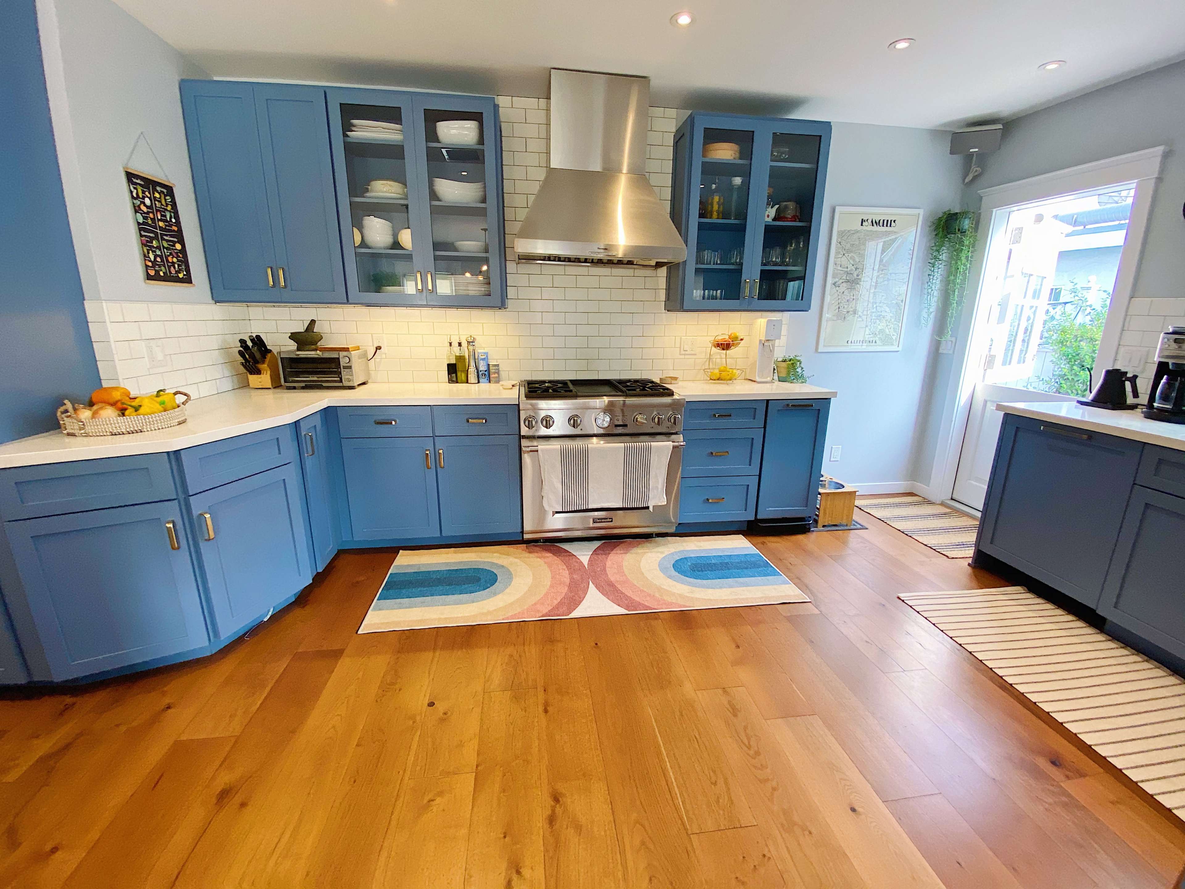 A modern kitchen features blue cabinetry, a stainless steel stove, and hardwood flooring, with large windows providing natural light.