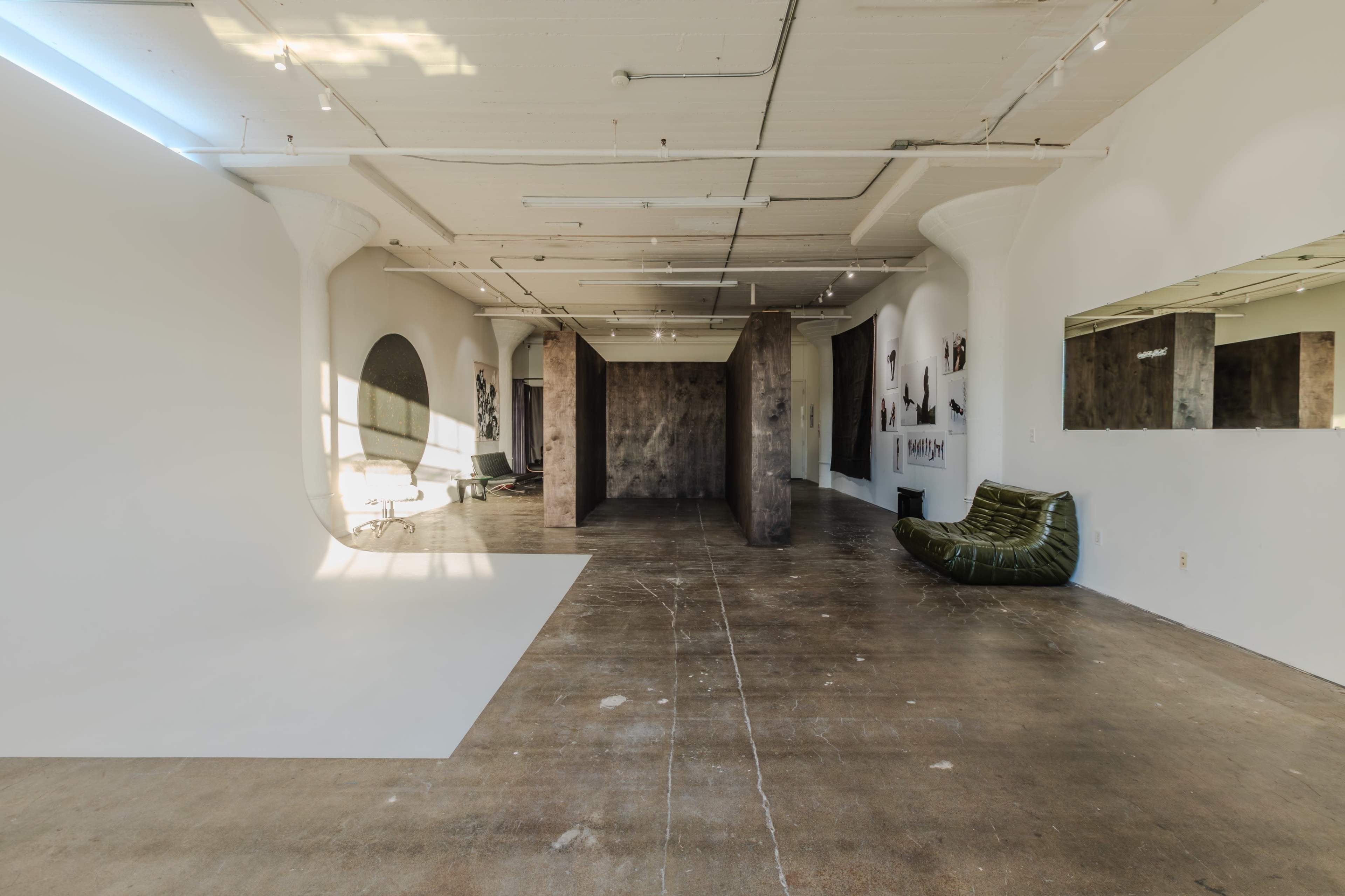 A spacious interior of a studio with concrete floors, white walls, and various seating arrangements, including a green sofa and a backdrop area.