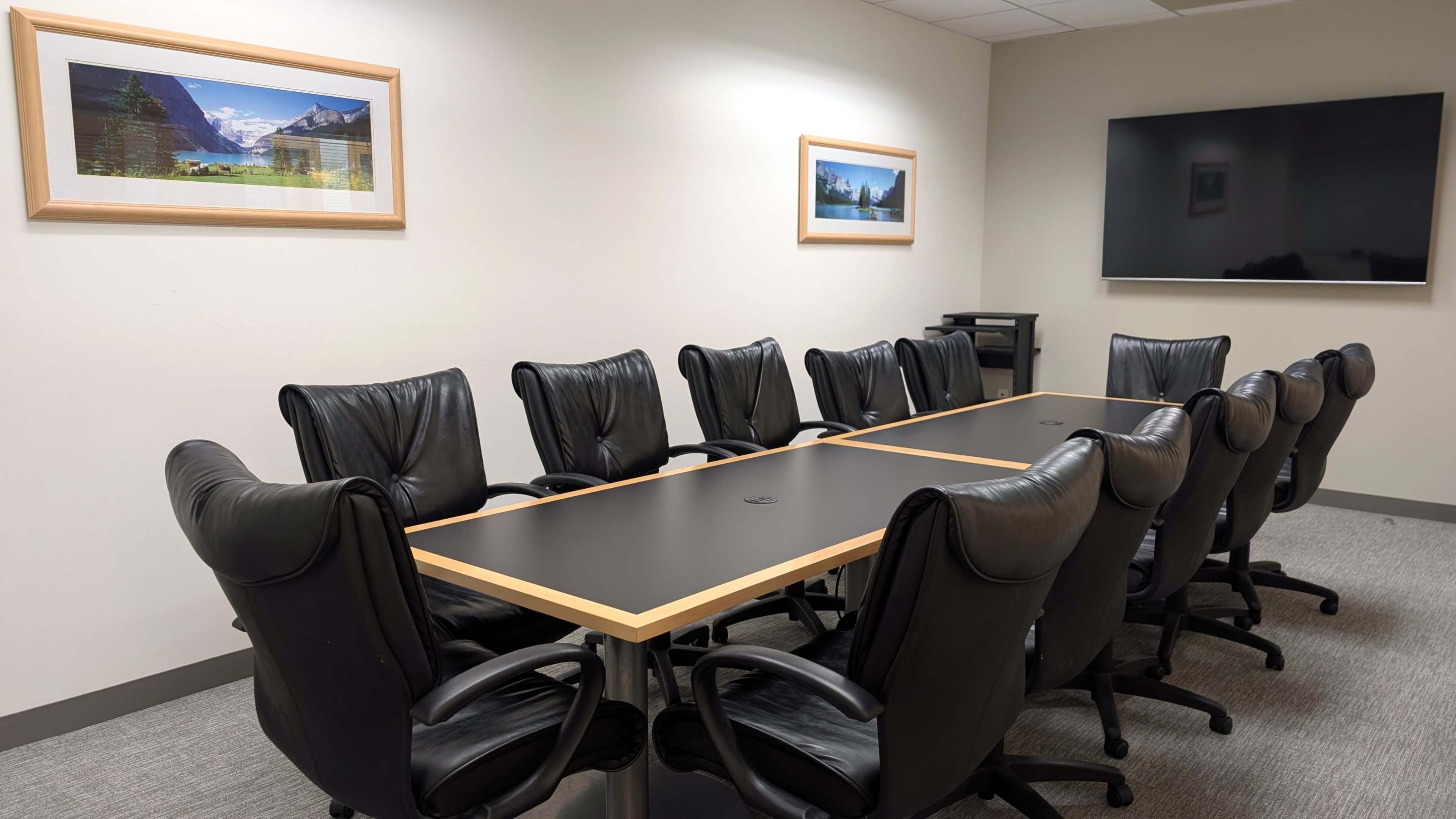 The image shows a conference room with a long table surrounded by black leather chairs, and two framed landscape pictures on the wall.