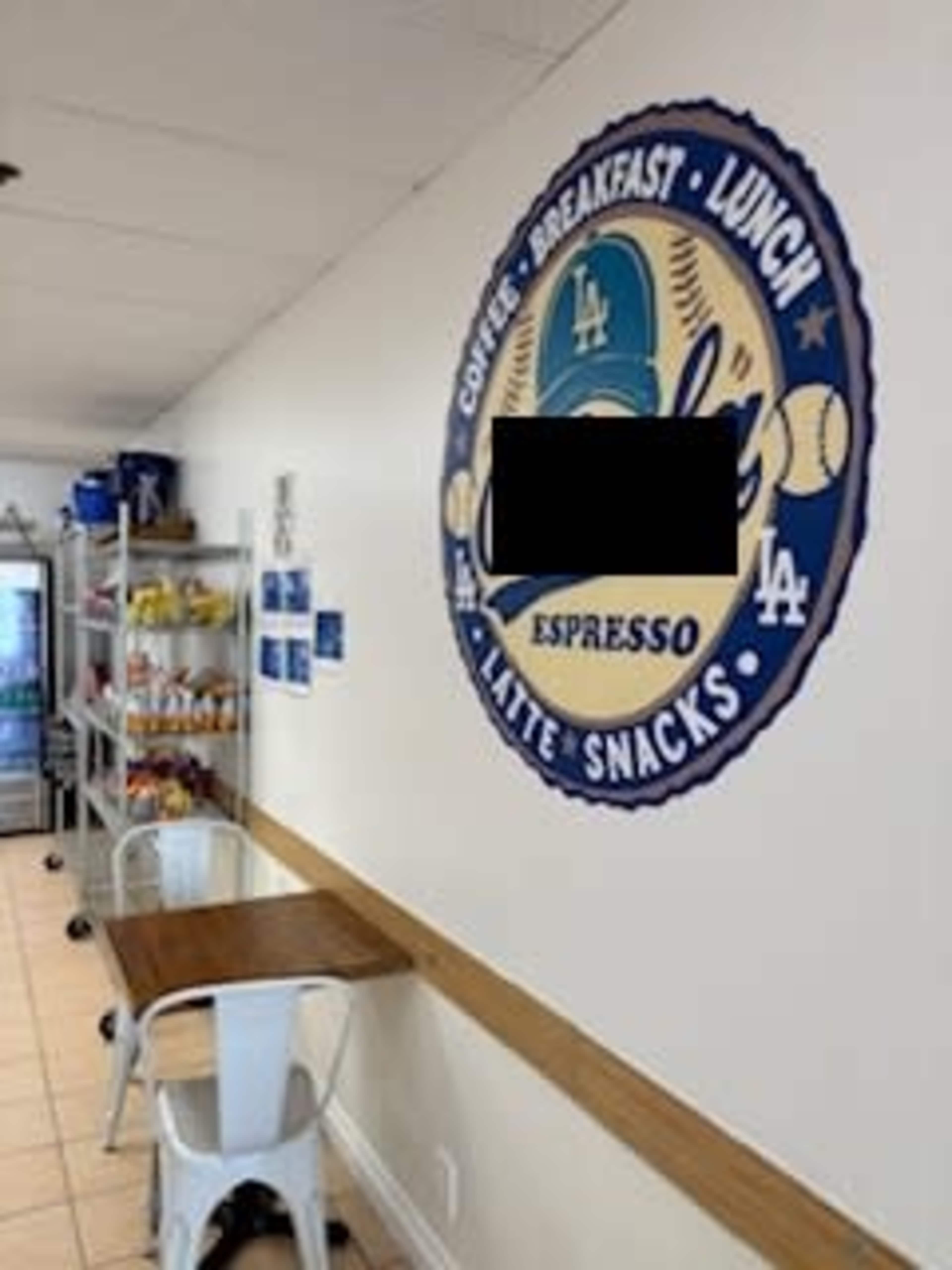 The image shows a café interior with a wall featuring a circular logo and text indicating offerings like coffee, breakfast, lunch, and snacks, alongside shelves stocked with beverages and food items.