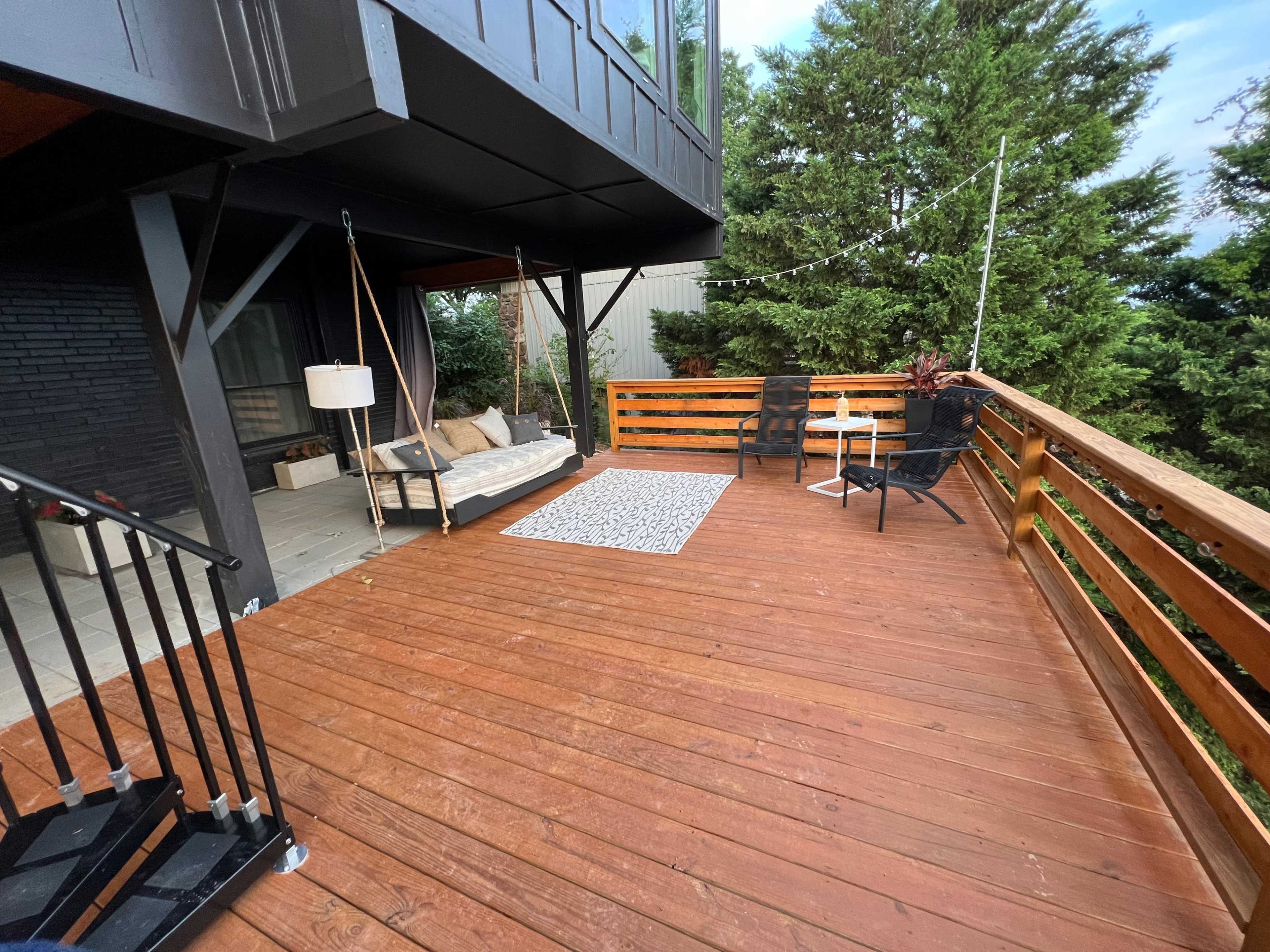 A wooden deck with seating, a rug, and greenery in the background.