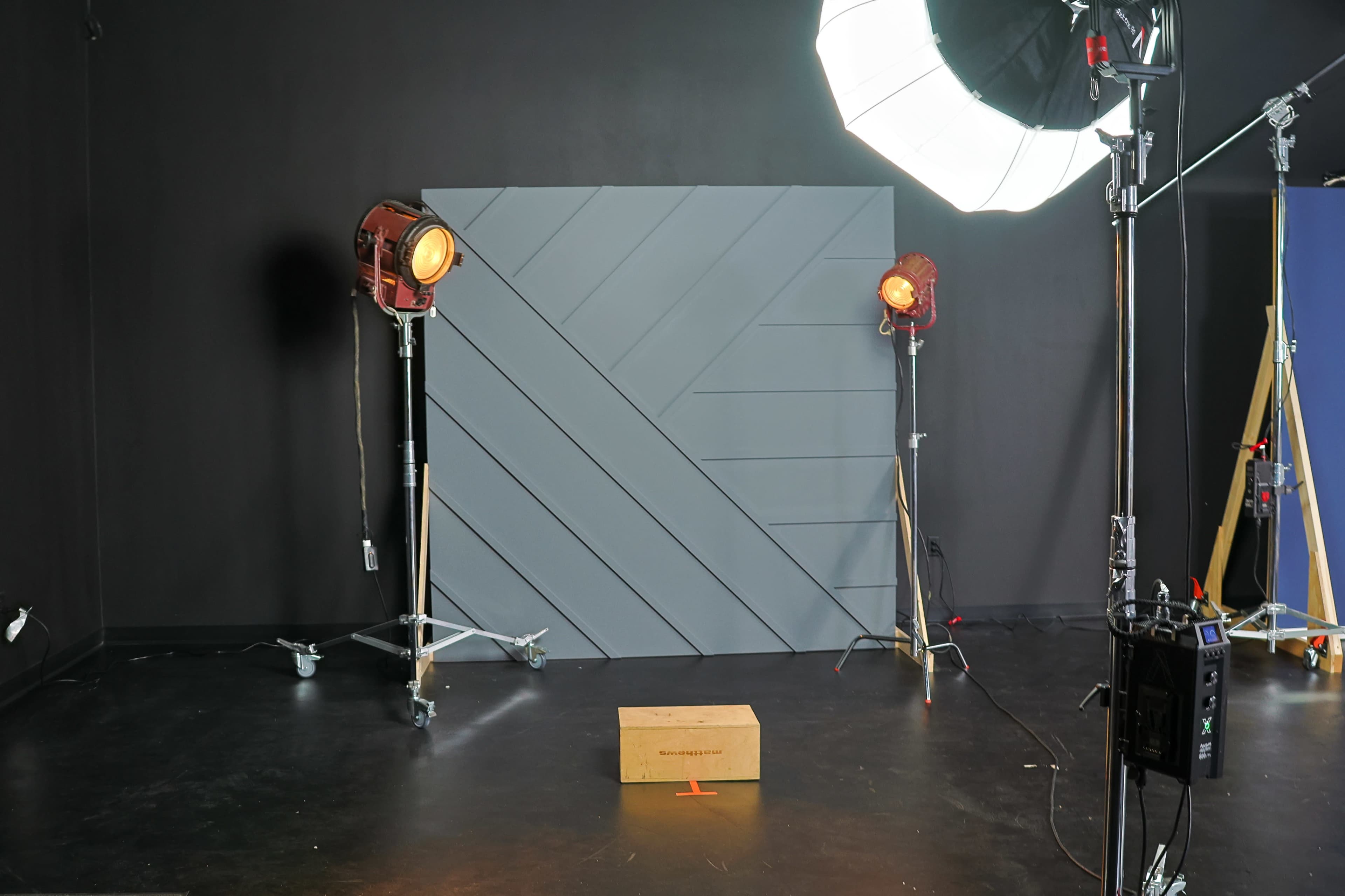 A photography studio setup with a gray backdrop, two stage lights on stands, and a wooden box placed in front of the backdrop.