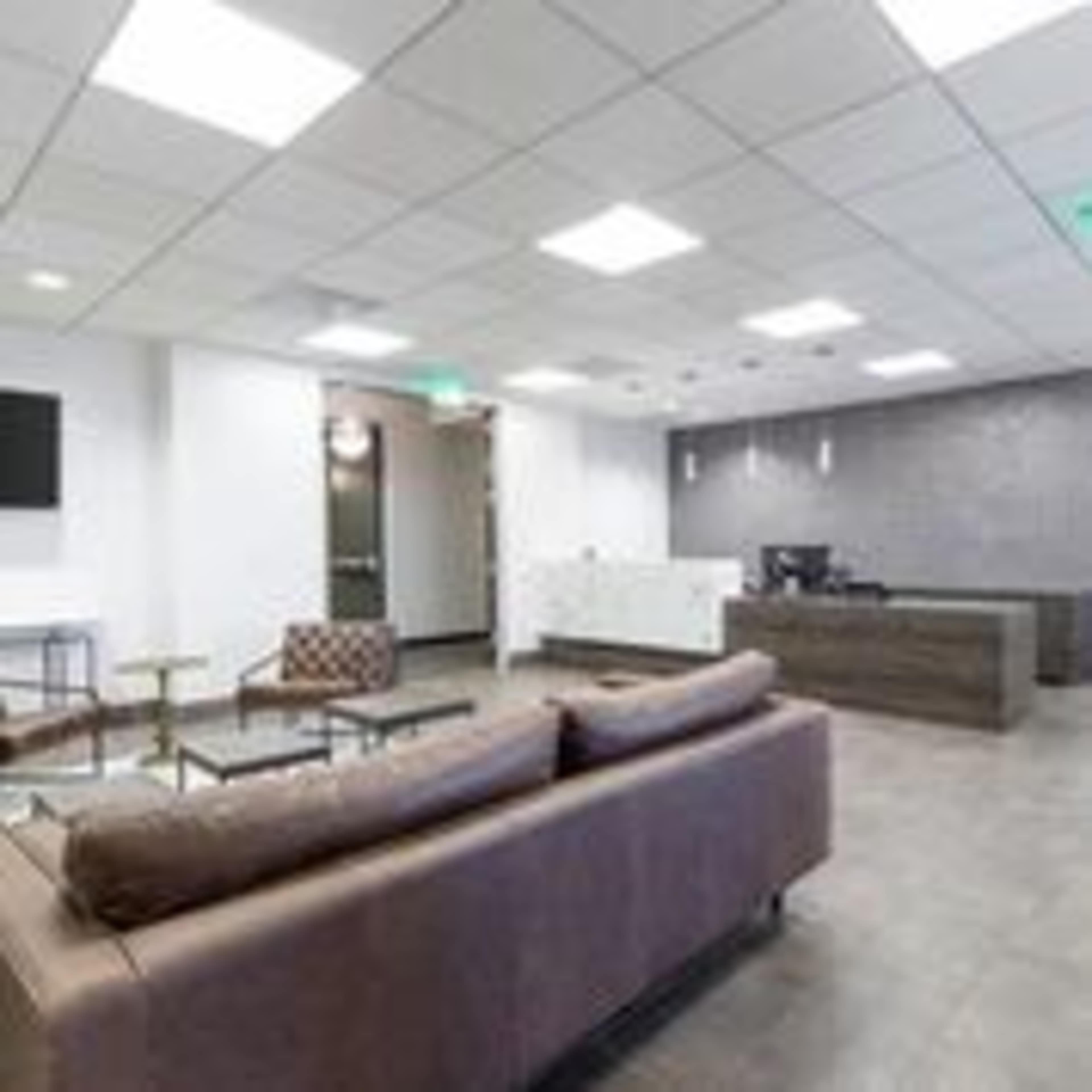 A modern office reception area with a seating area, a reception desk, and a television on the wall.