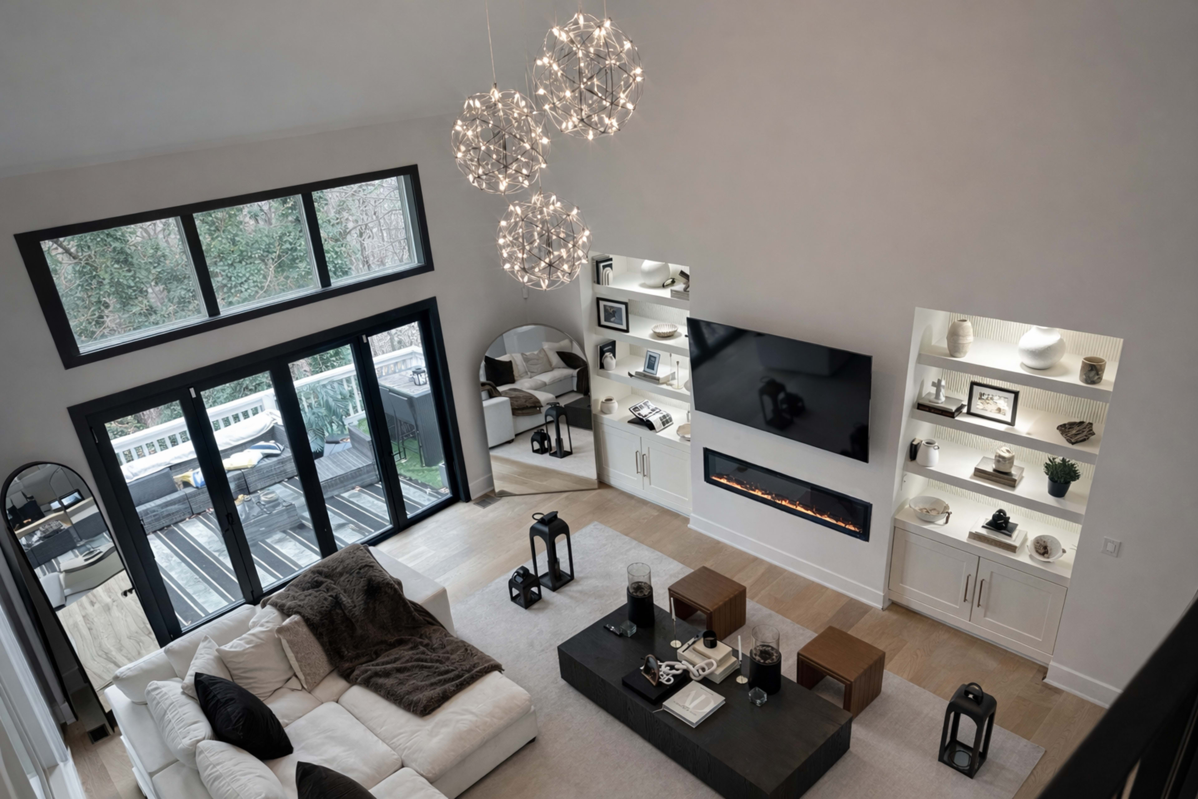 The image shows a modern, bright living room with a large TV mounted on the wall, an electric fireplace, and a seating area arranged around a coffee table.