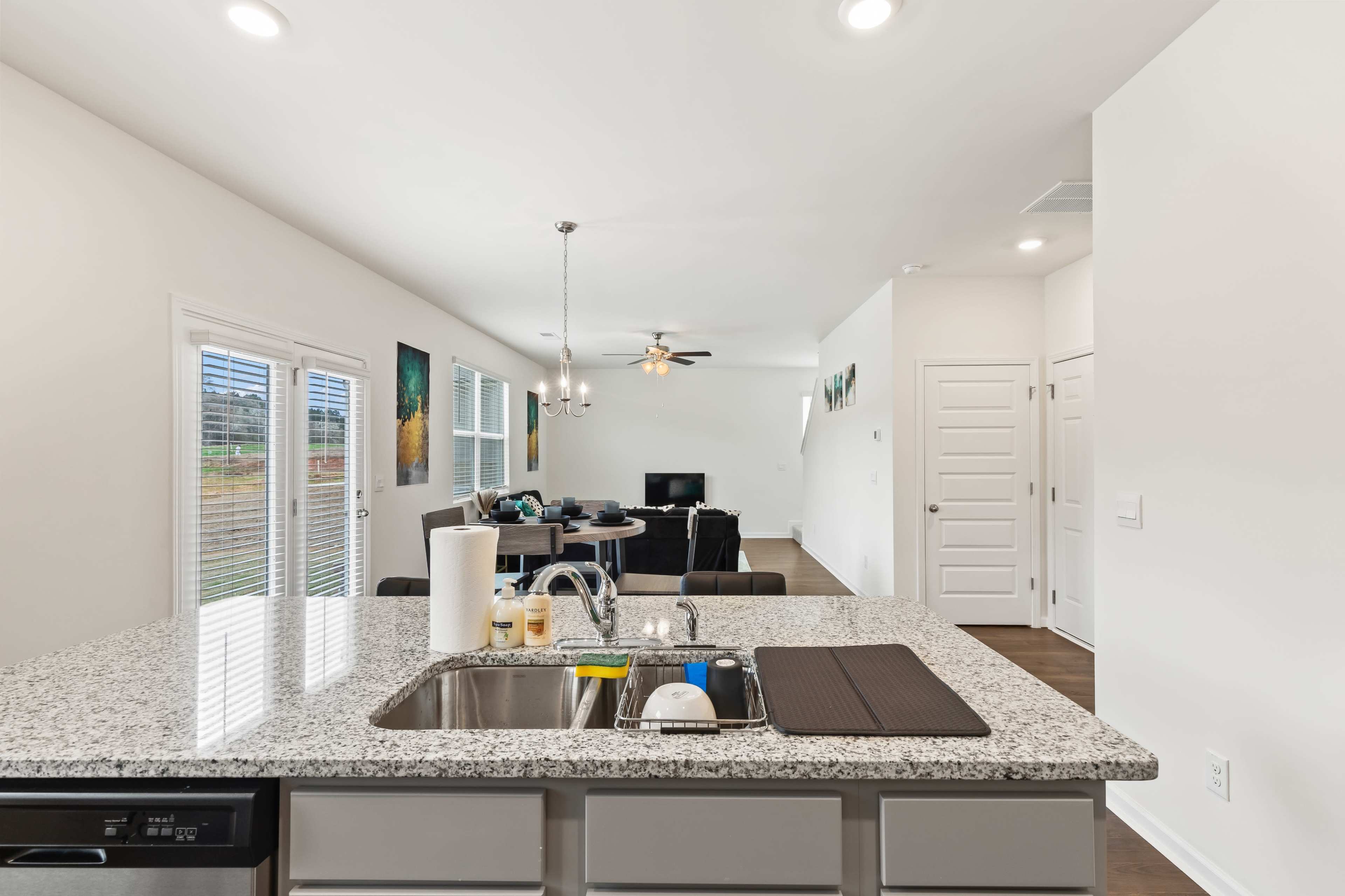 A modern kitchen island with a granite countertop, facing an open living area furnished with a sofa, a ceiling fan, and a television.