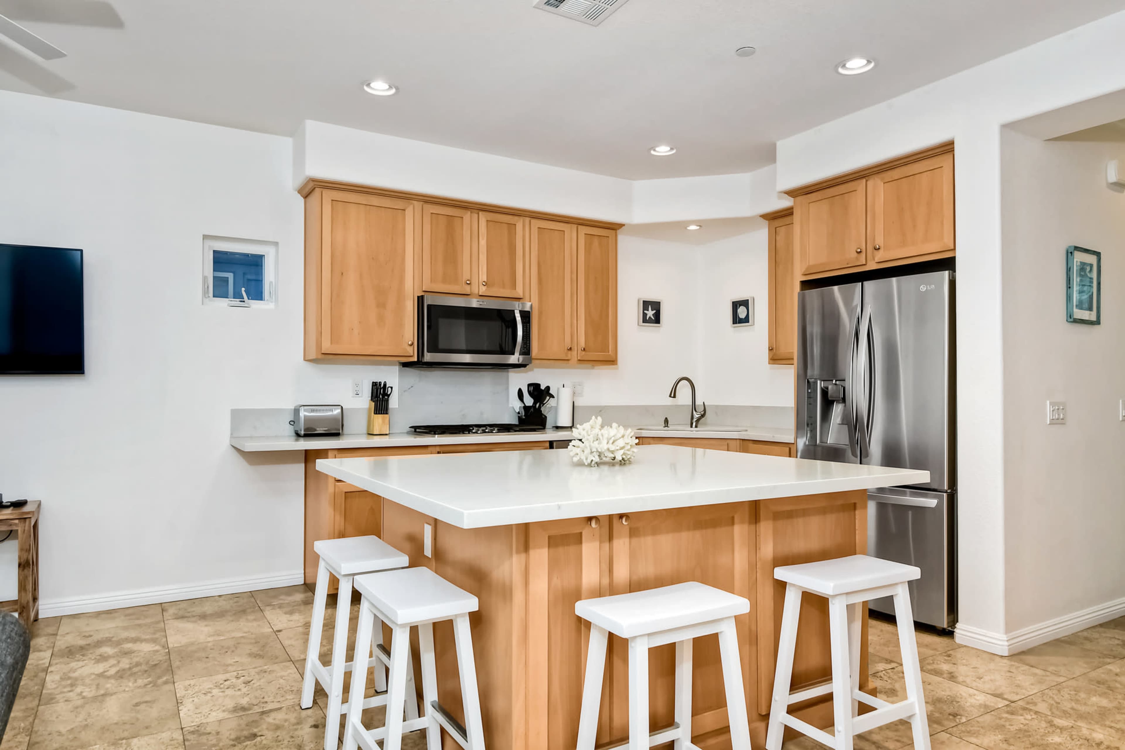 A modern kitchen with wooden cabinets, stainless steel appliances, and a central island with four white stools.