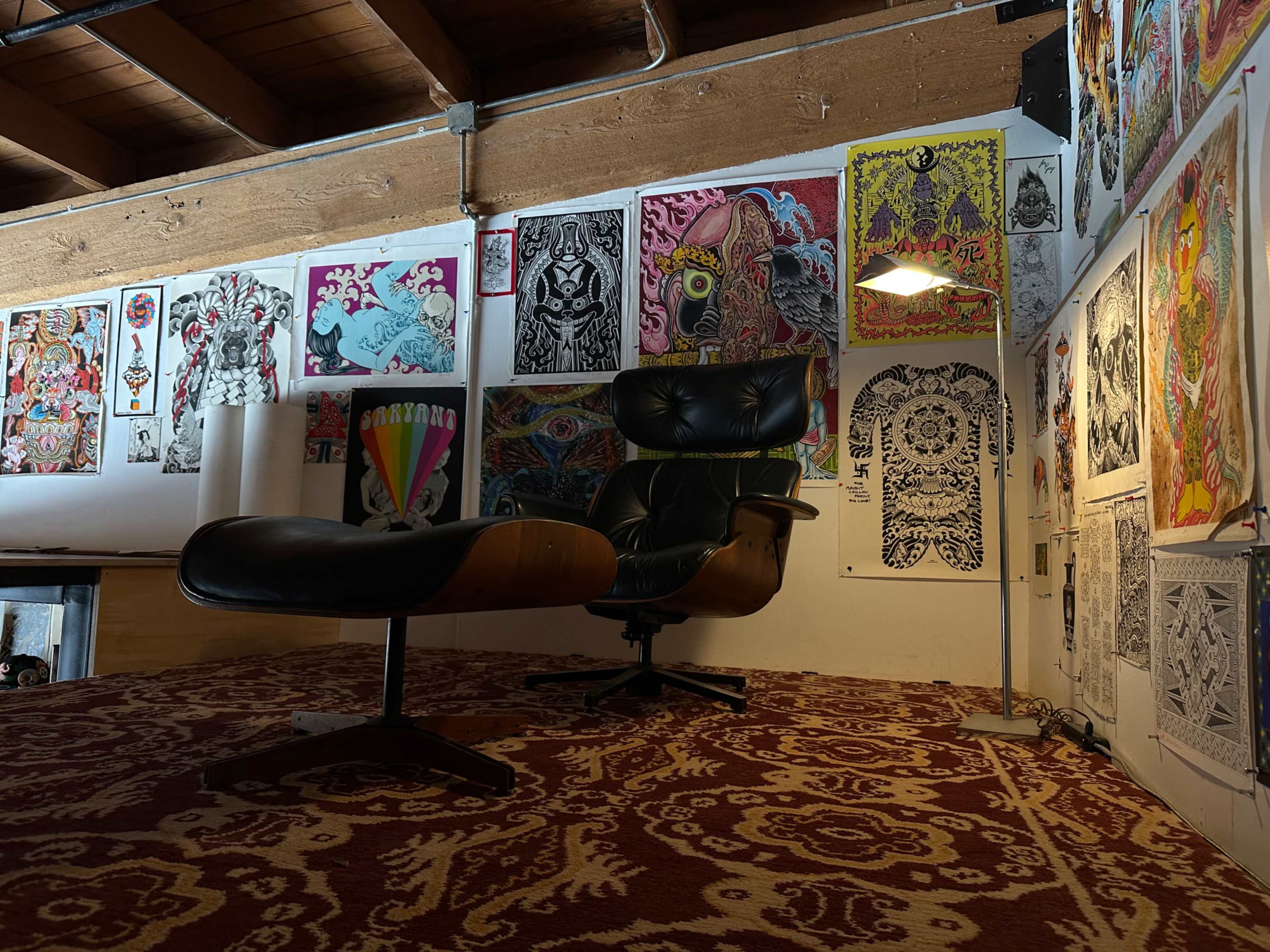 The image shows a modern lounge area with an Eames chair and ottoman, surrounded by colorful artworks displayed on the walls.