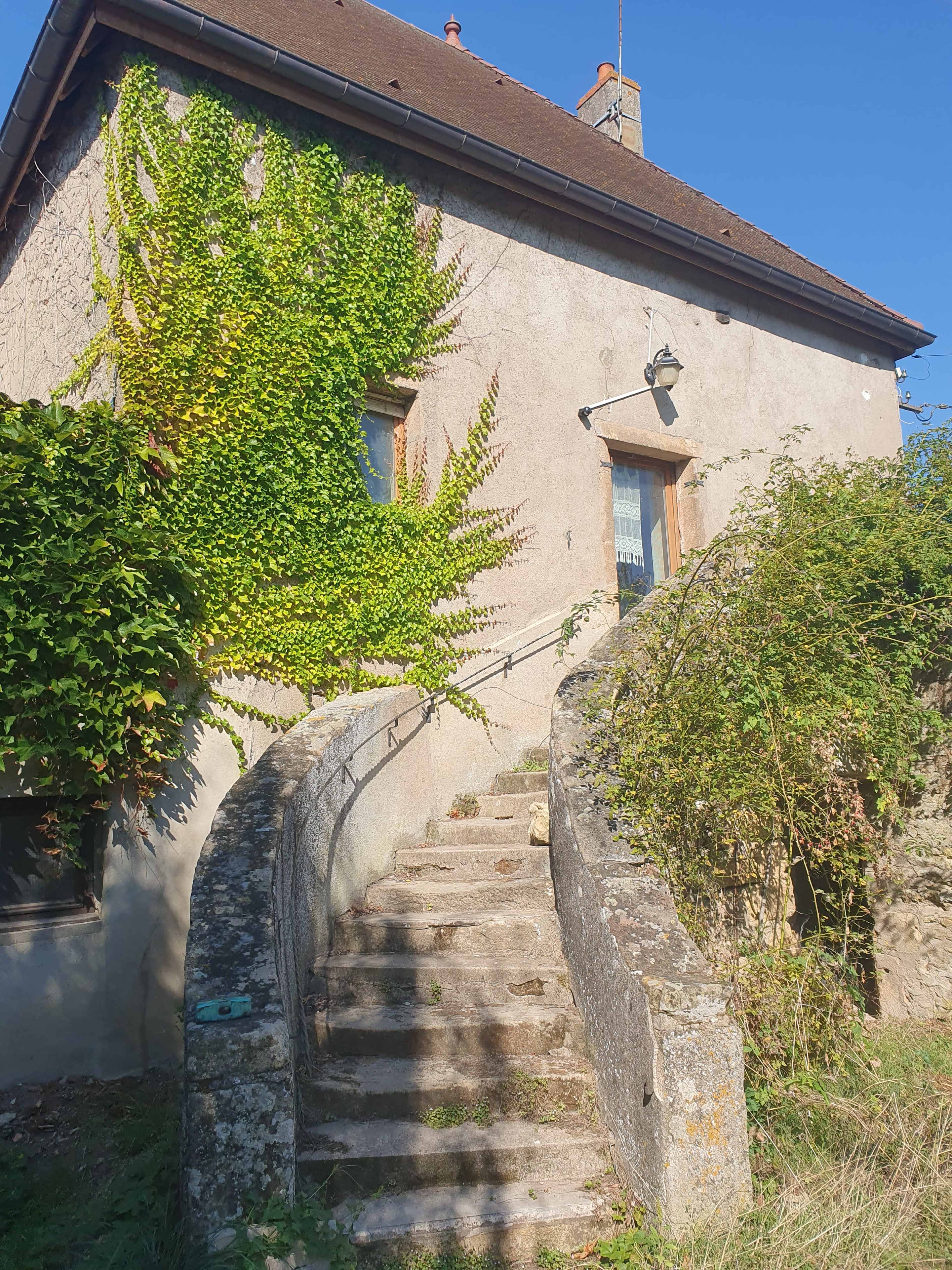 A stone staircase leads up to a house with ivy-covered walls and a clear blue sky above.