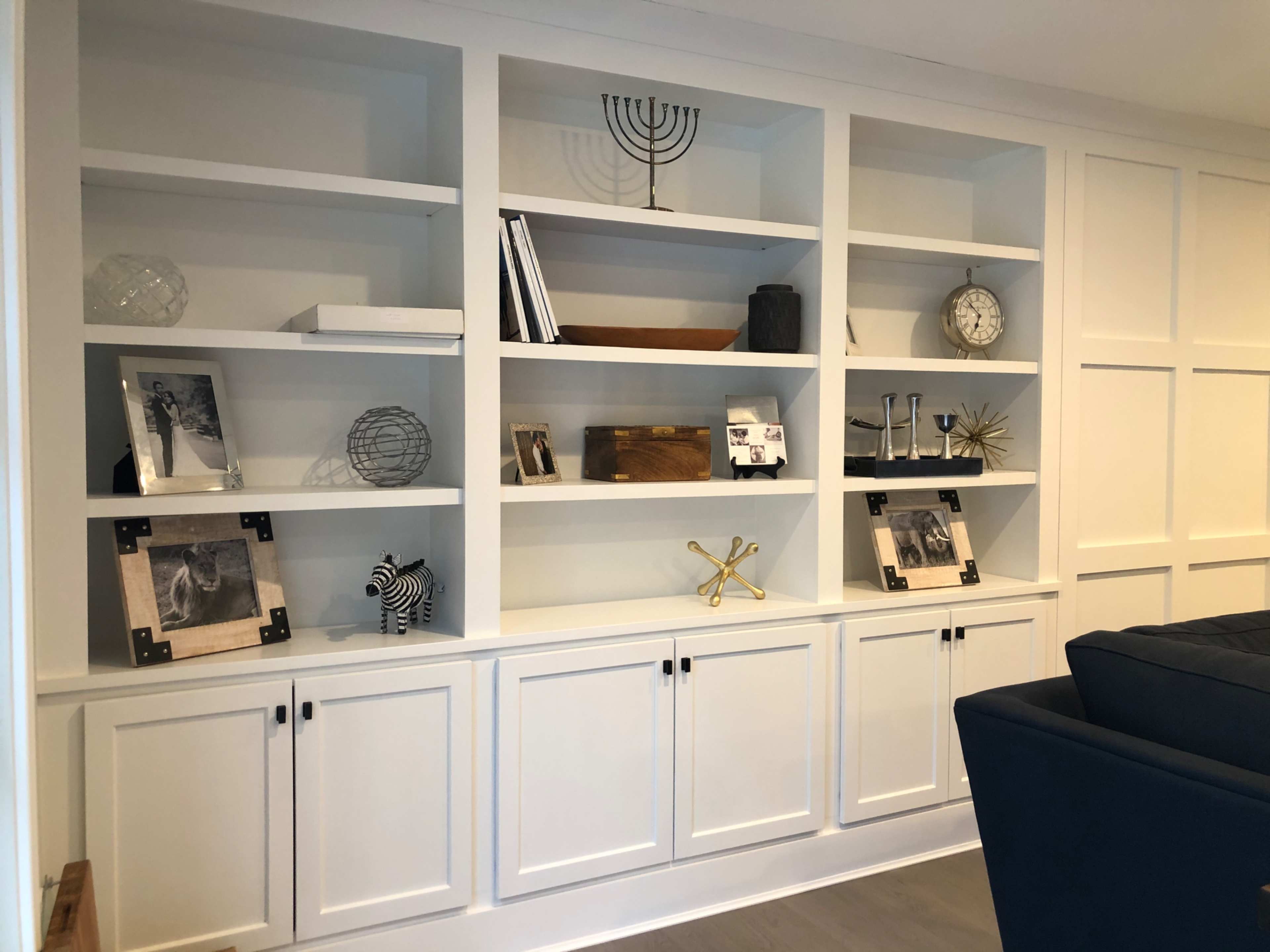 A white shelving unit filled with various decorative objects, books, and picture frames, arranged neatly with closed cabinets below.