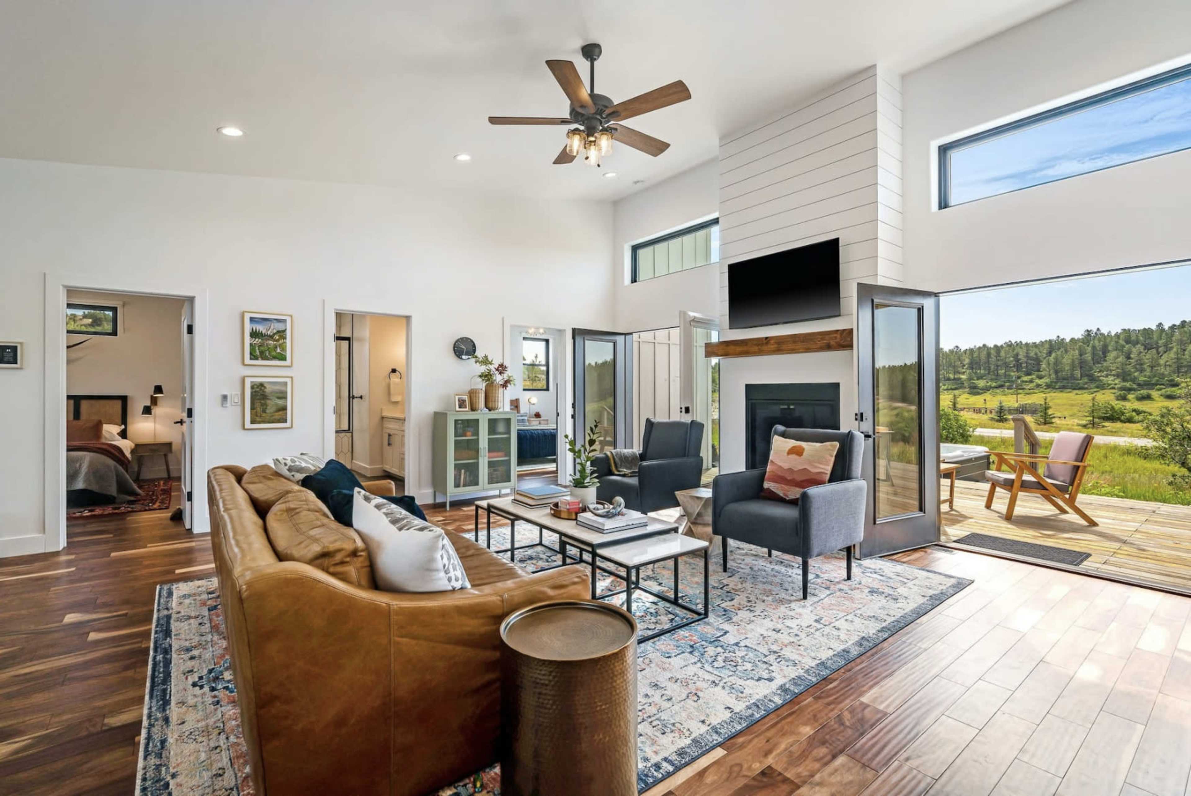 A modern living room with a leather couch, two armchairs, a coffee table, and large windows overlooking a scenic outdoor view.