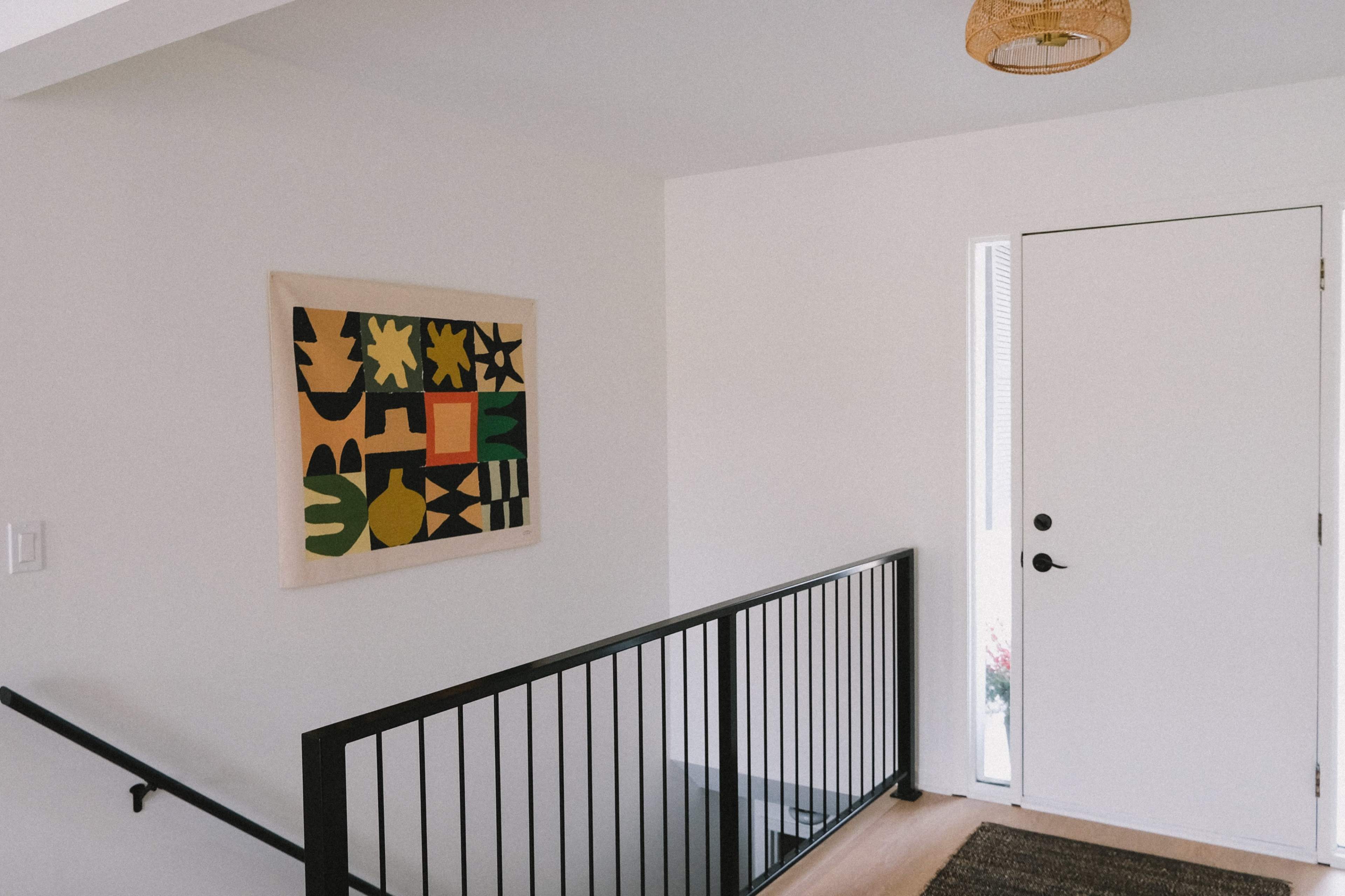 A staircase leads to a landing with a colorful abstract painting on the wall next to a white door.