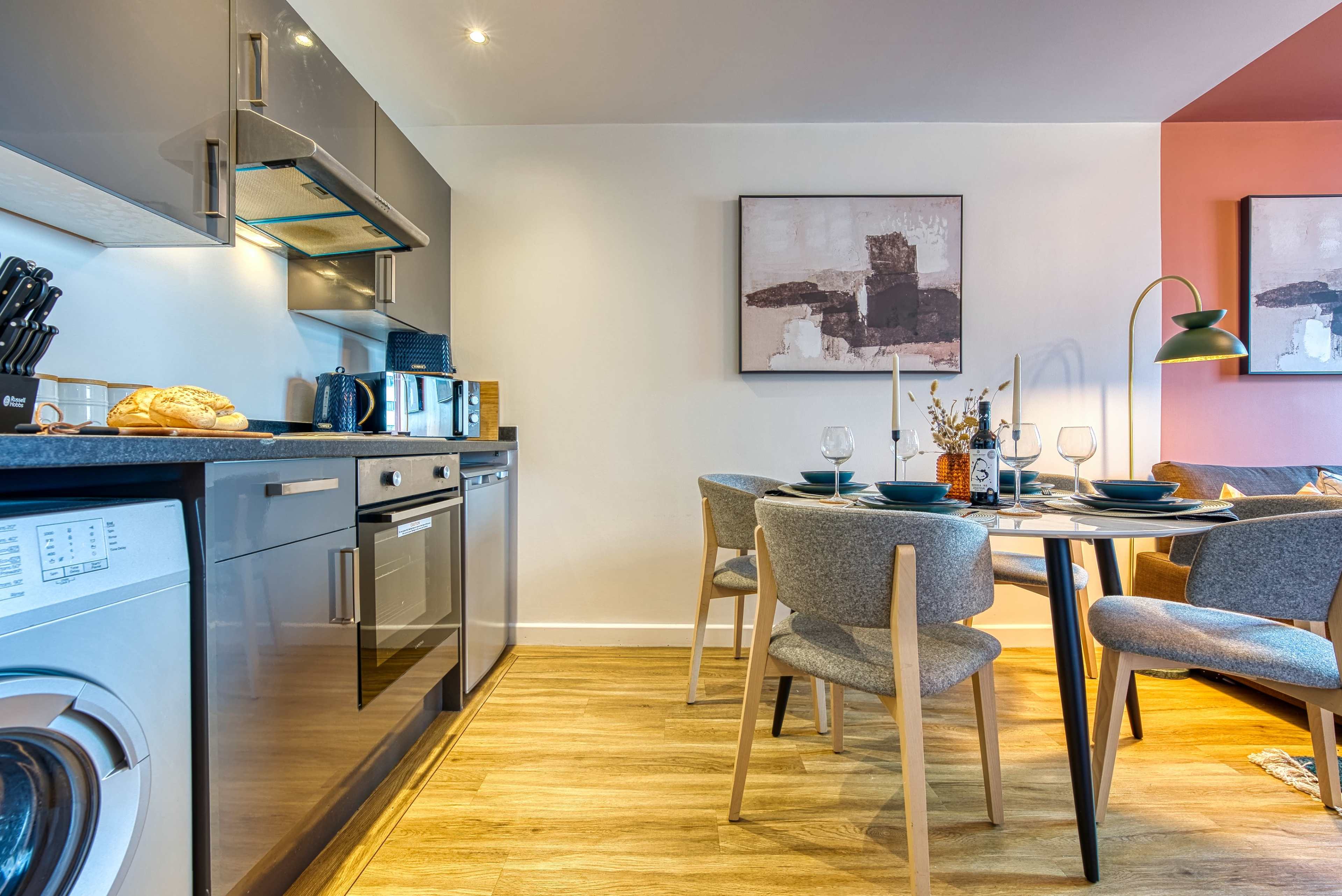 A modern kitchen and dining area with stainless steel appliances, a round dining table, and stylish gray chairs.