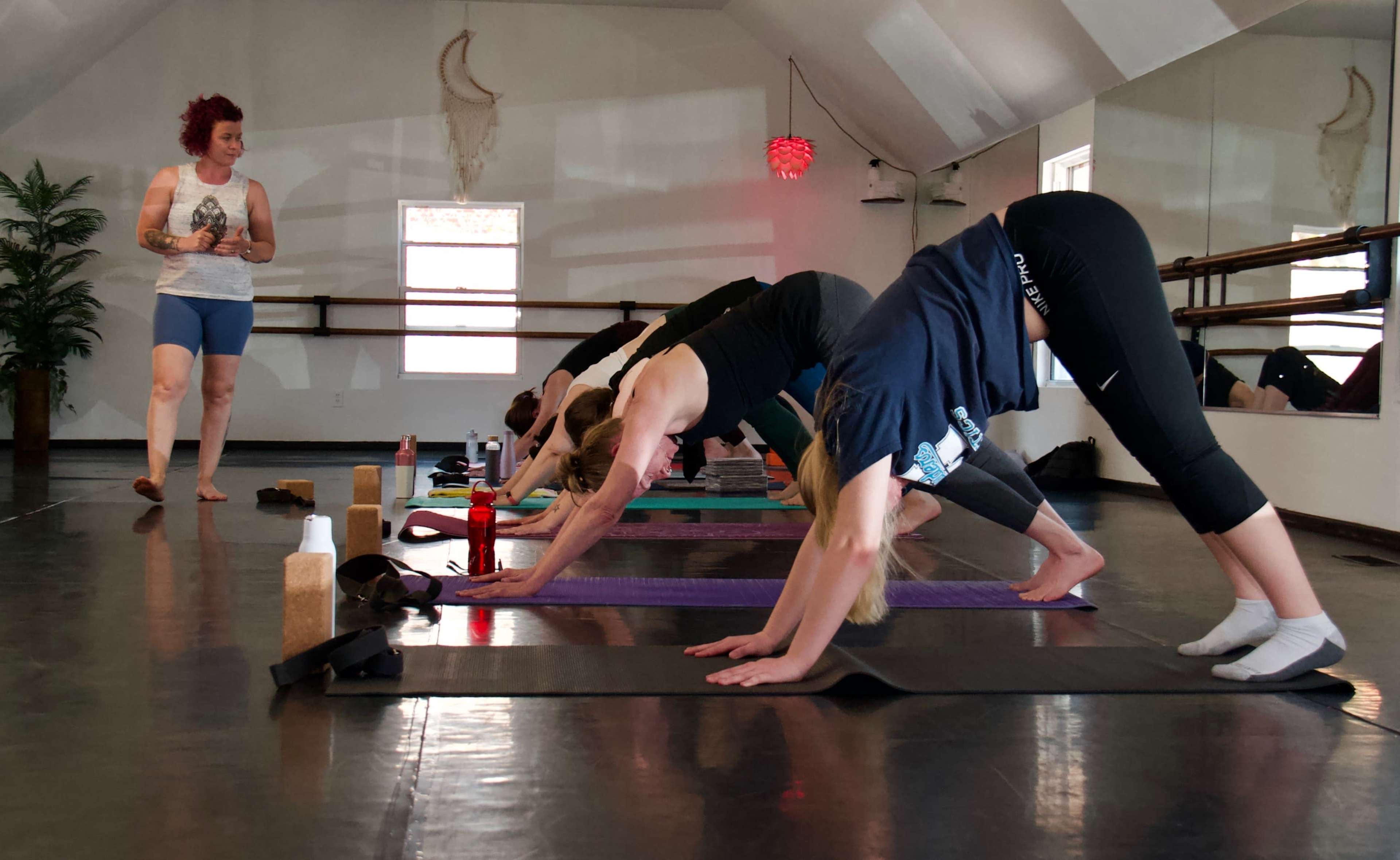 A group of people practice yoga on mats in a bright studio while an instructor guides them.