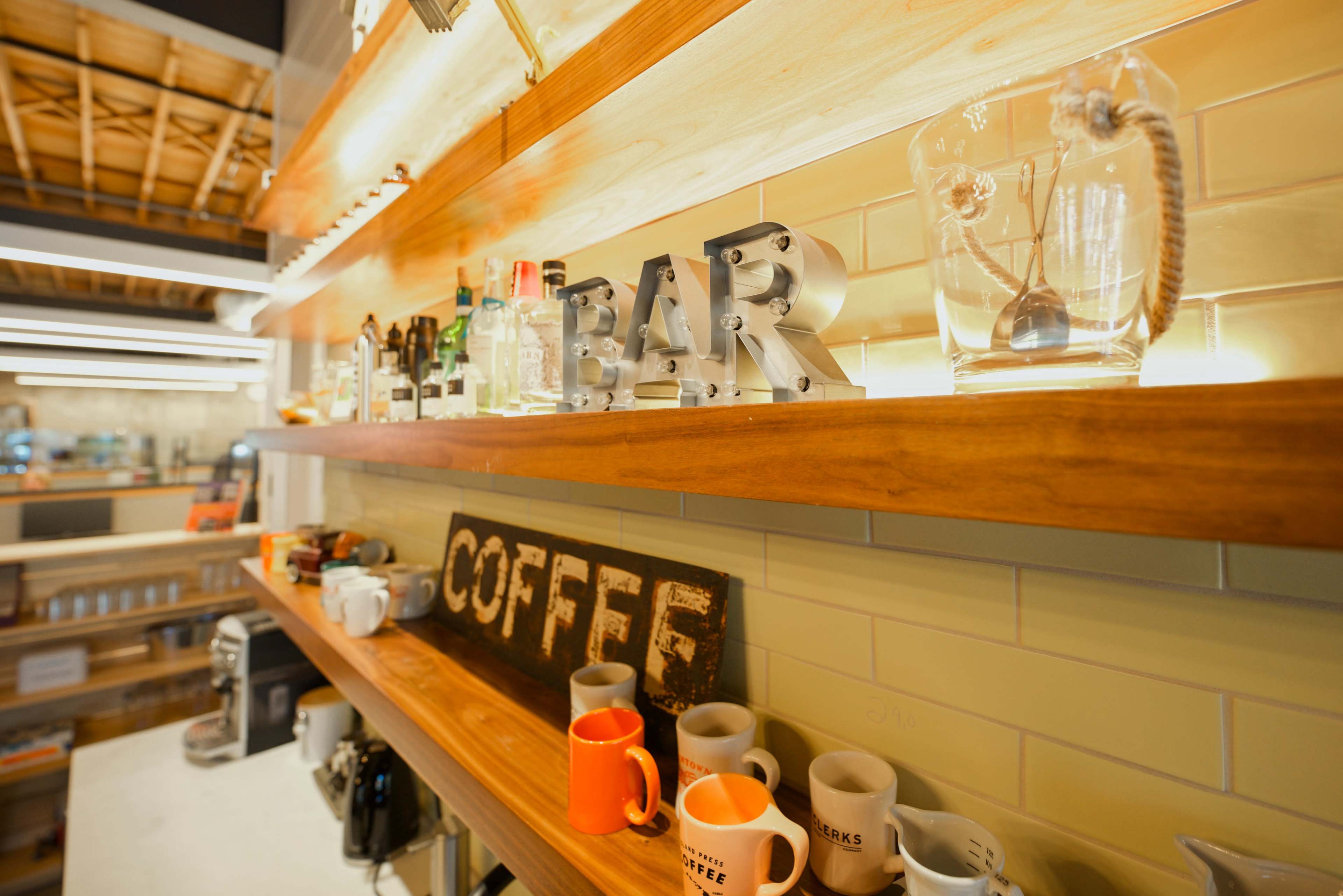 A wooden shelf displaying various bottles, mugs, and a sign that reads "COFFEE" in a well-lit space.