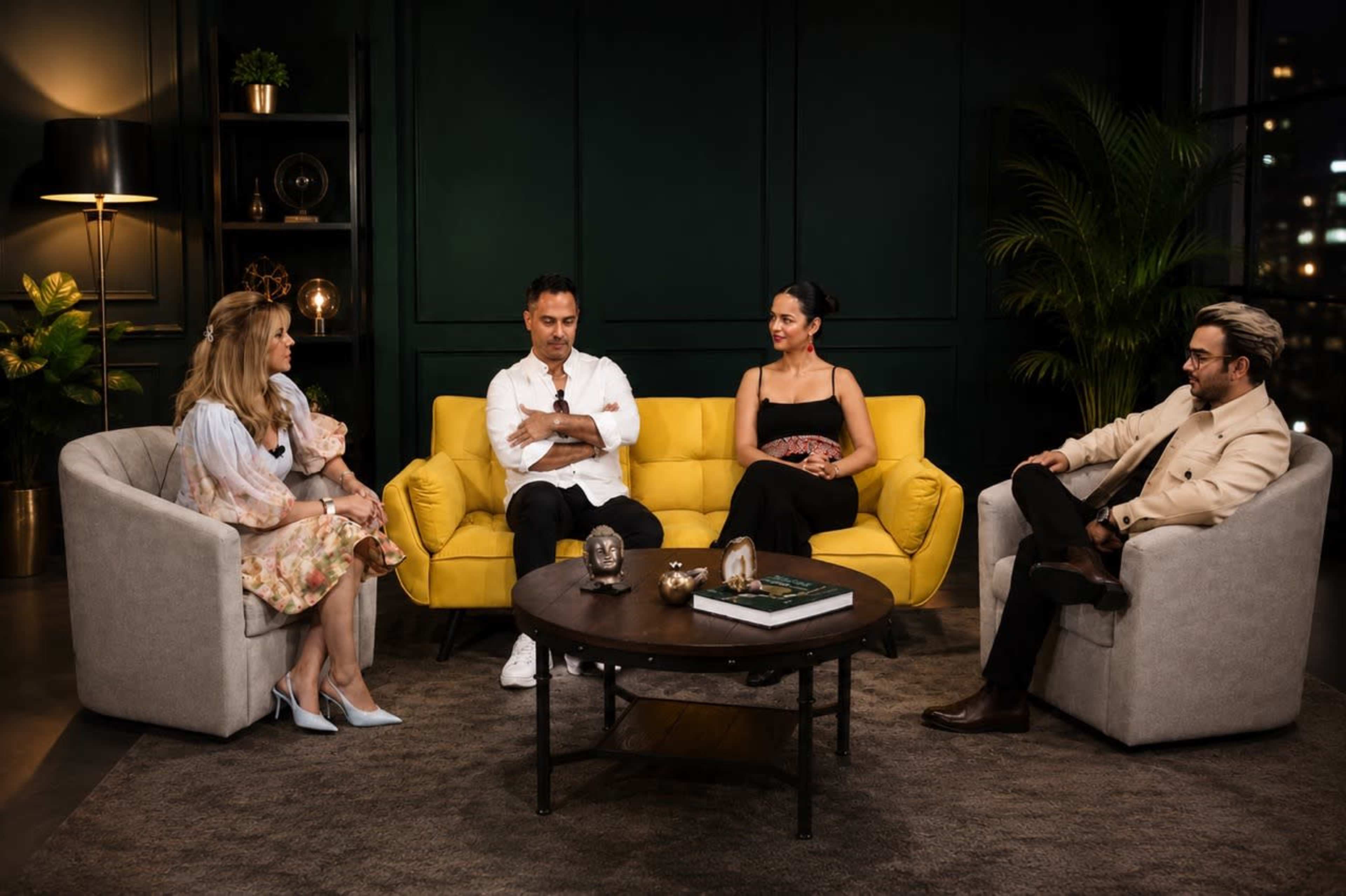 A group of four people is seated on a yellow couch in a modern living room with soft lighting and a coffee table in front of them.