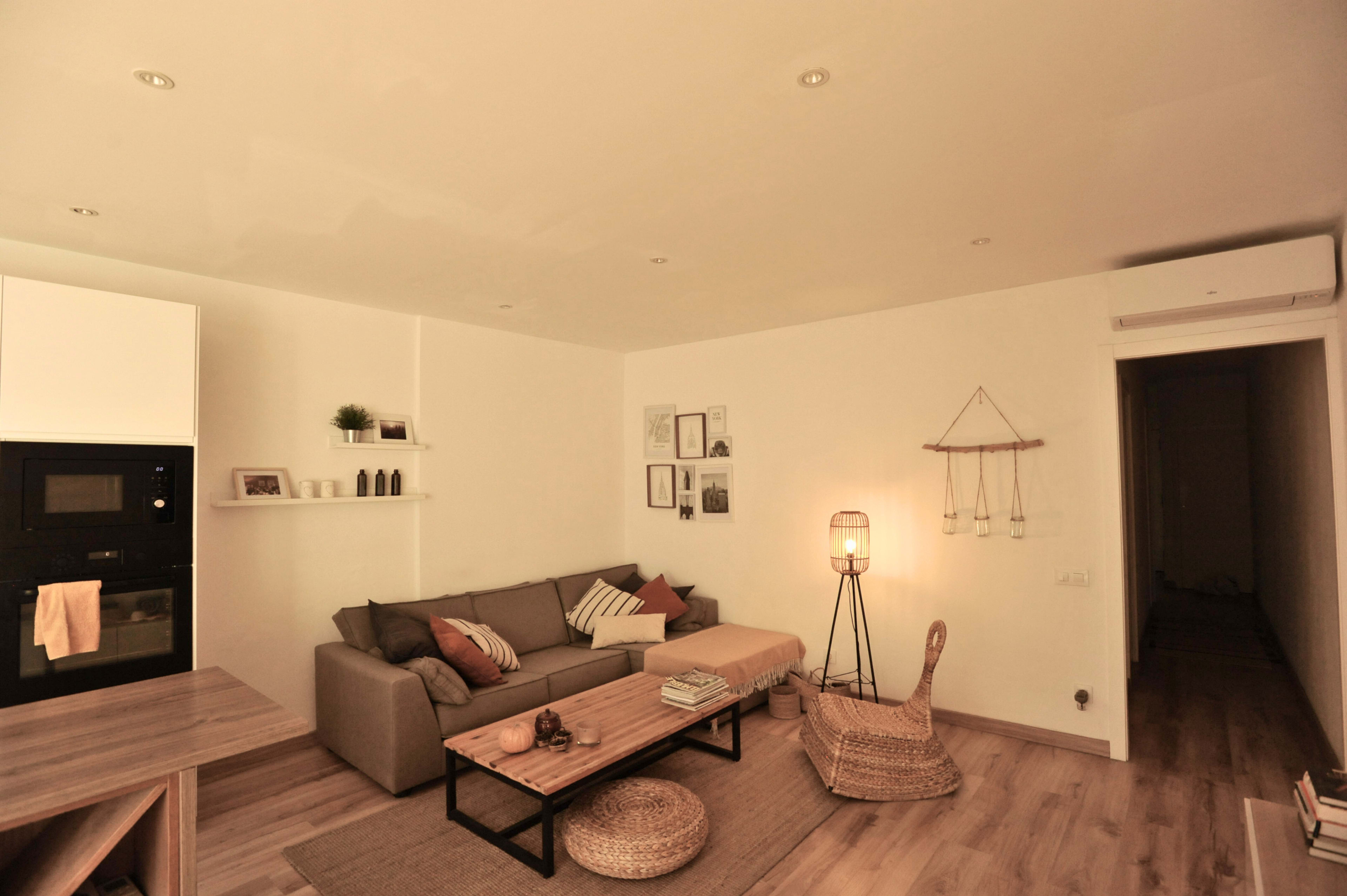 The image shows a modern, minimalist living room featuring a gray sofa, a wooden coffee table, a woven chair, and wall decor.