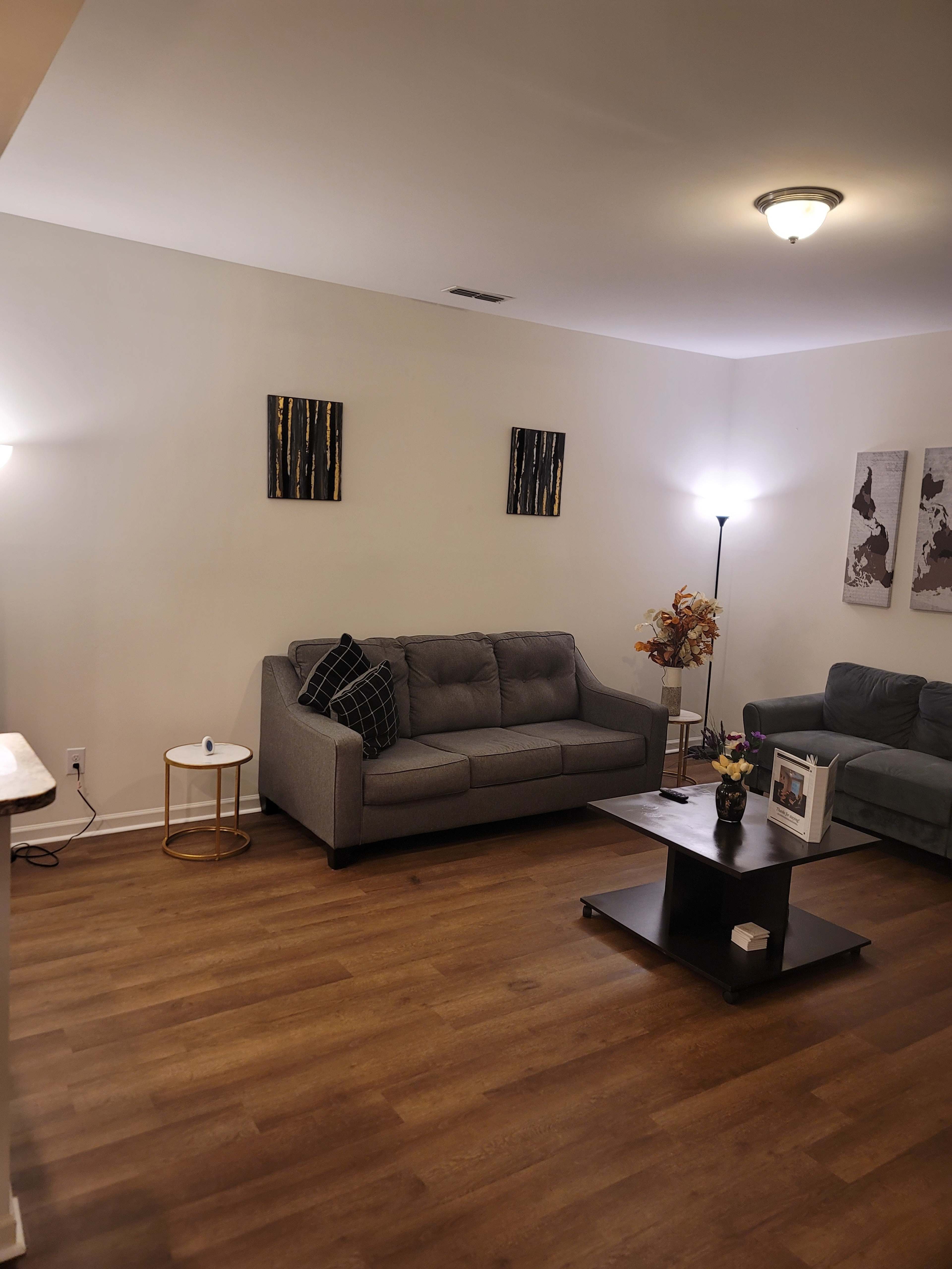 A living room with two sofas, a coffee table, and decorative wall art, illuminated by two lamps.