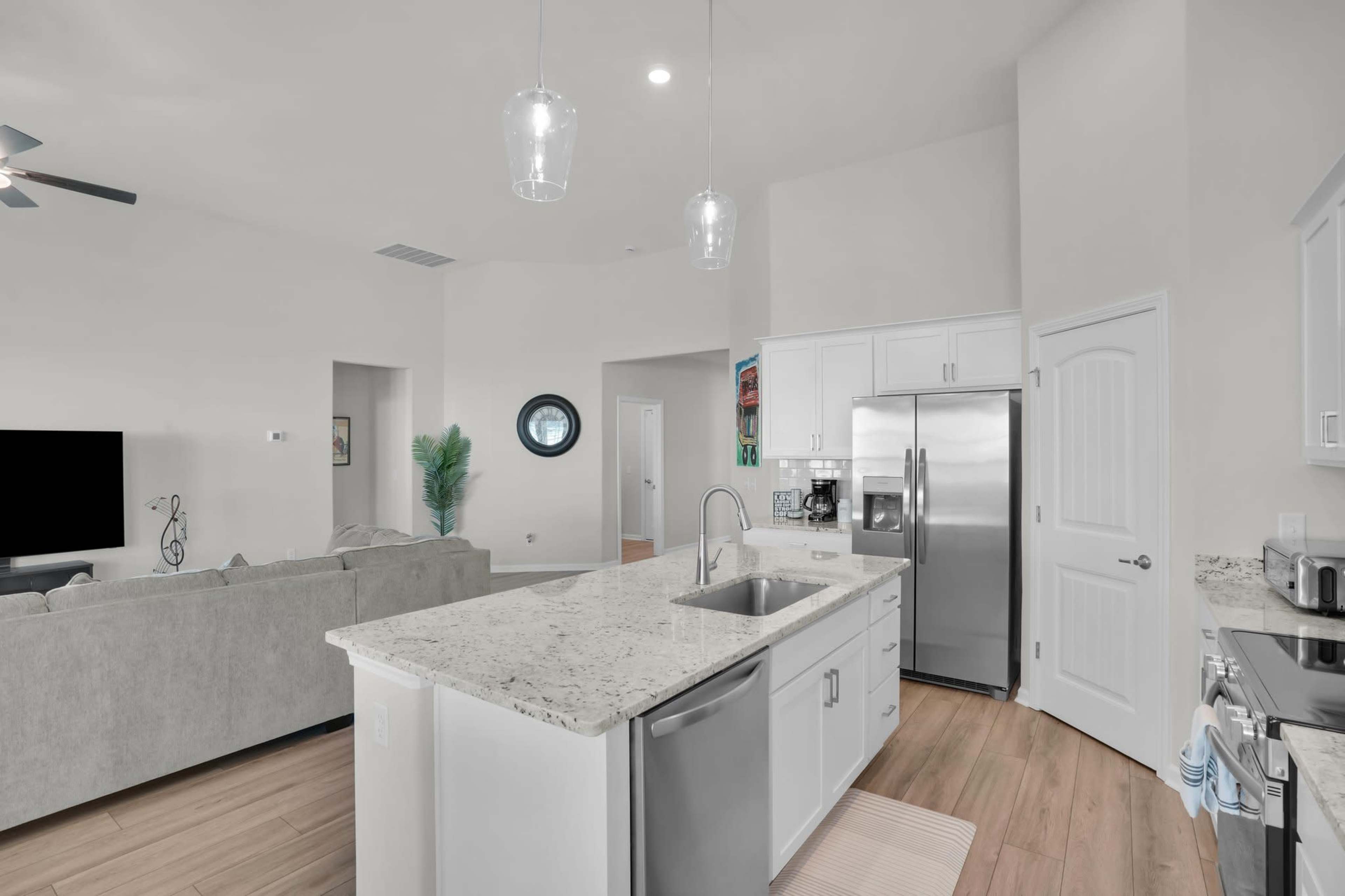 The image shows a modern kitchen with granite countertops, stainless steel appliances, and an open layout connecting to a living area.