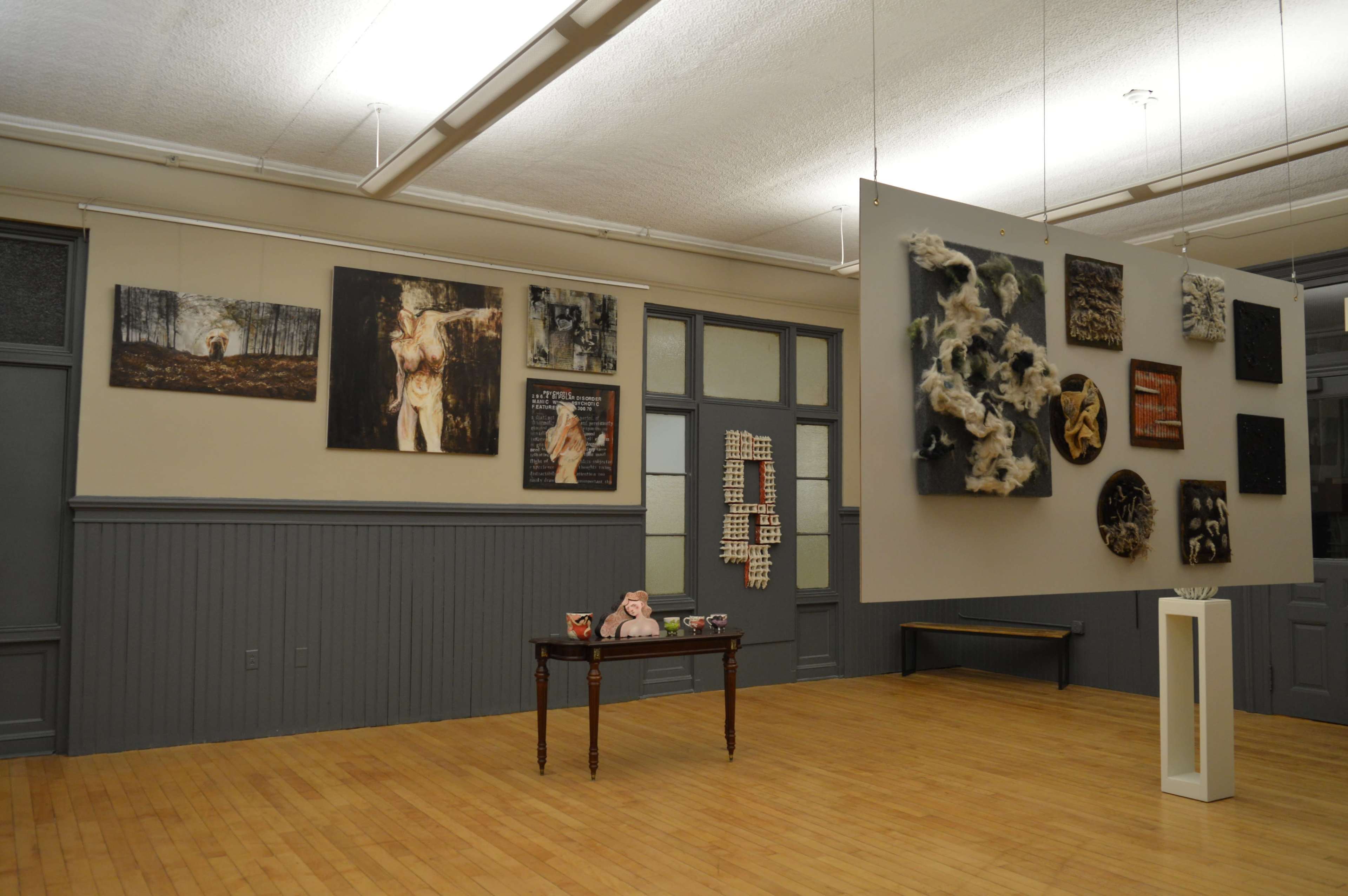 An art gallery featuring a variety of framed artworks on the walls and a small table displaying decorative items in the center.