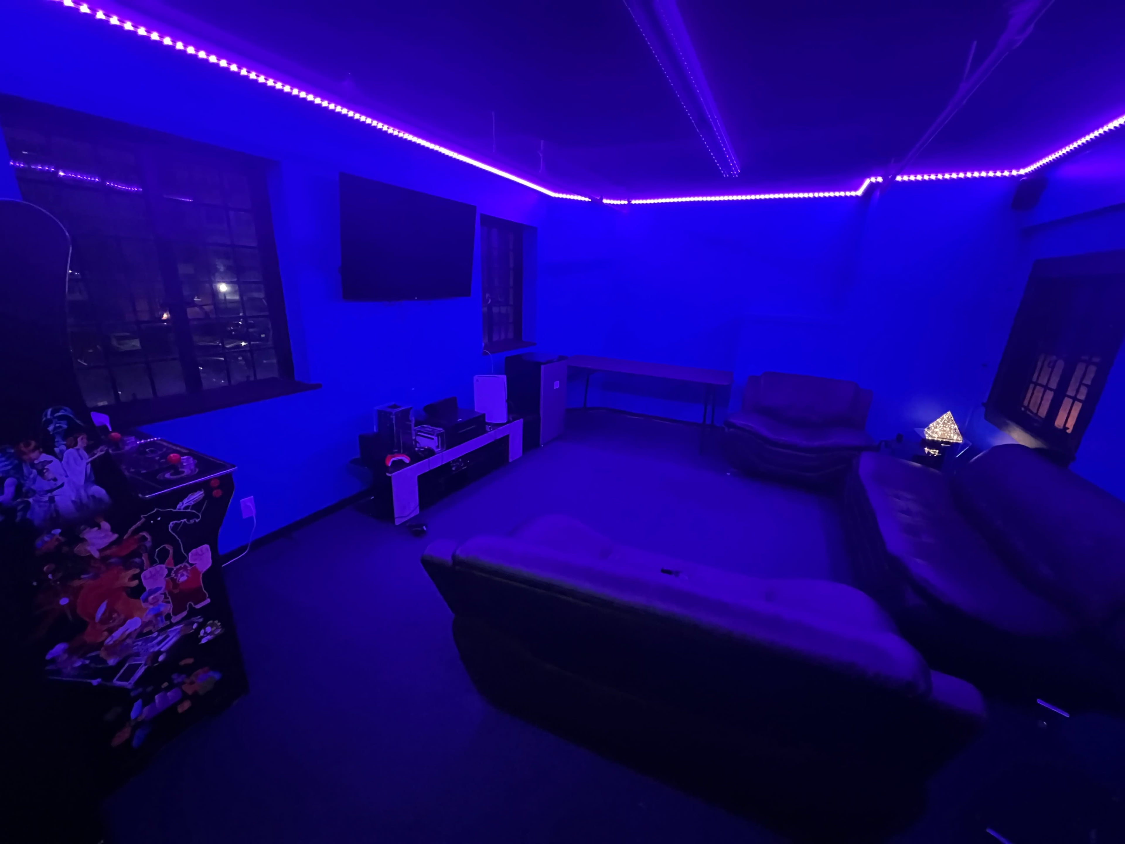 The room features blue walls and neon lighting, with two couches and a television mounted on the wall.