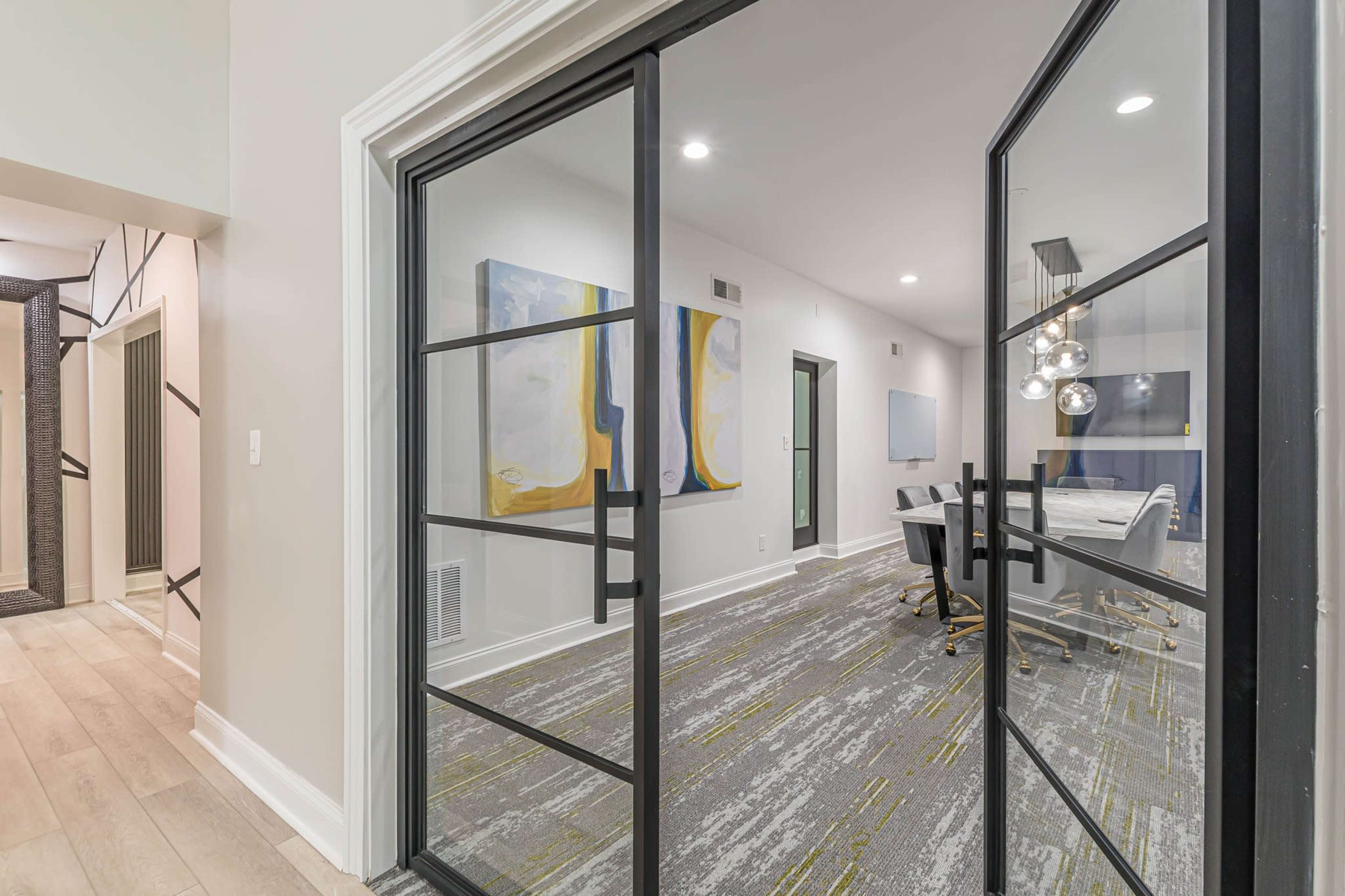 A modern conference room visible through glass doors, featuring a large table surrounded by chairs and abstract artwork on the walls.