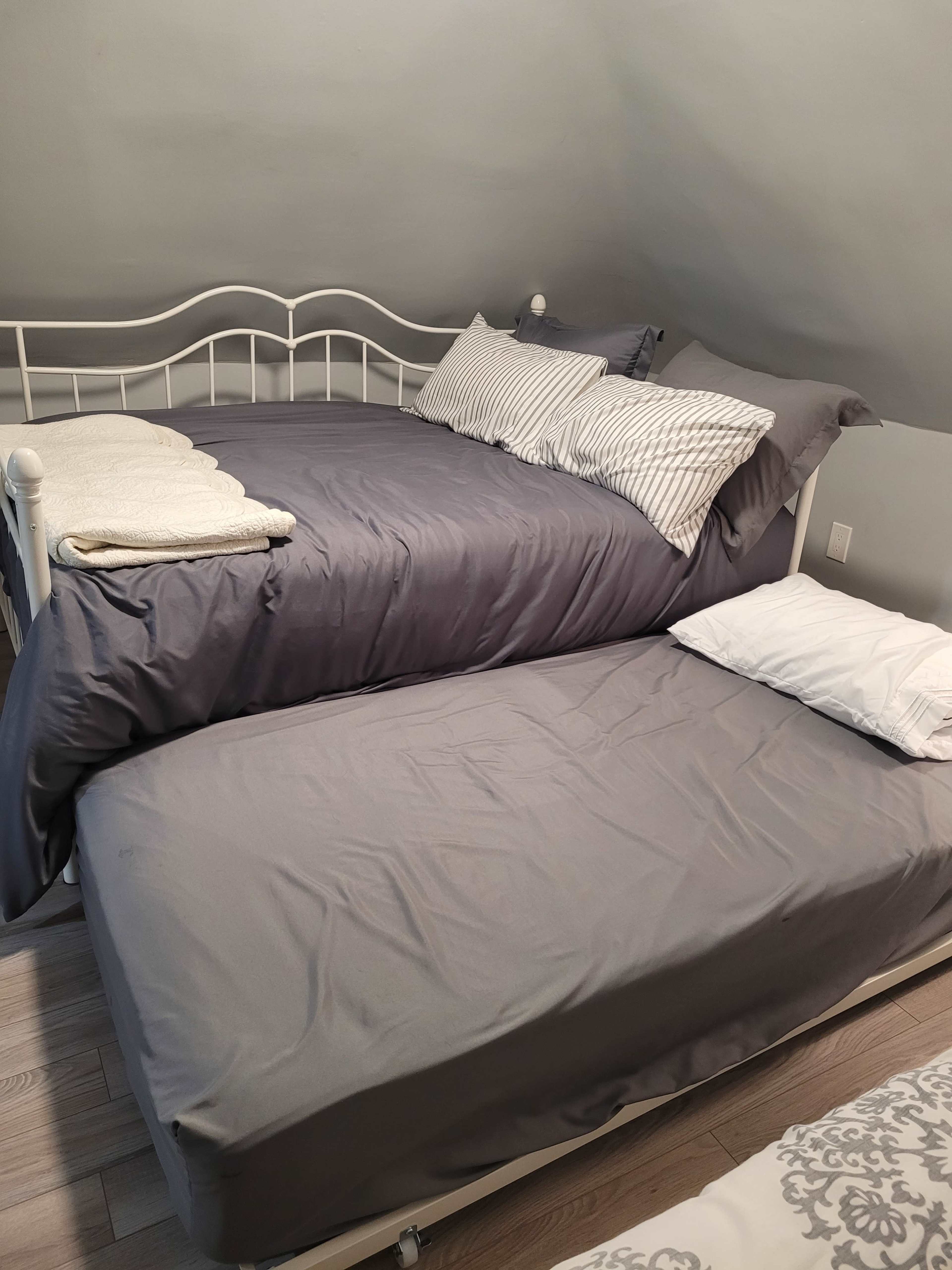 A lofted bed with a lower pull-out mattress, both covered in gray bedding with white pillows.