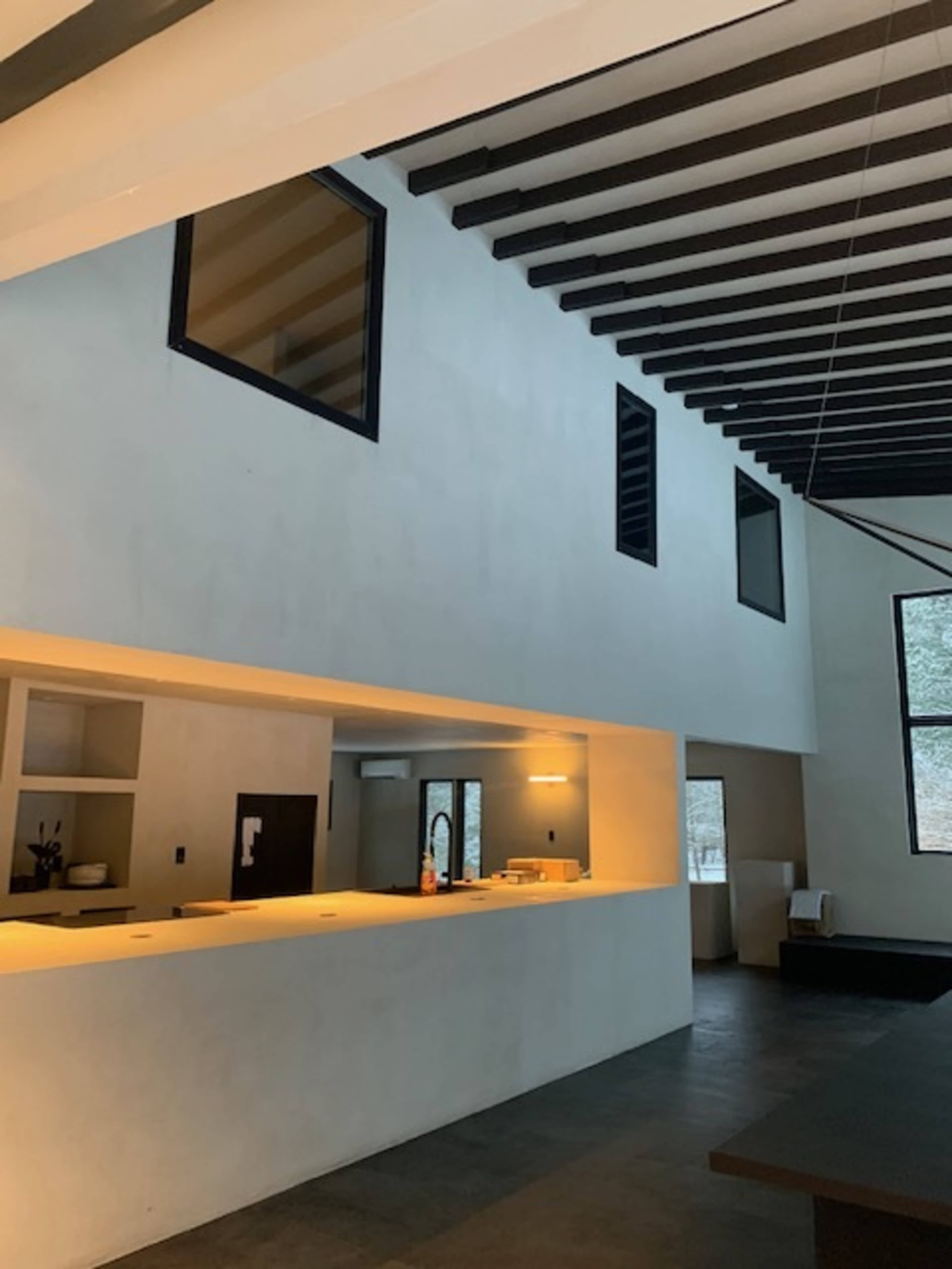 The image shows an interior of a modern space featuring high ceilings, exposed wooden beams, and large windows that allow light to enter.