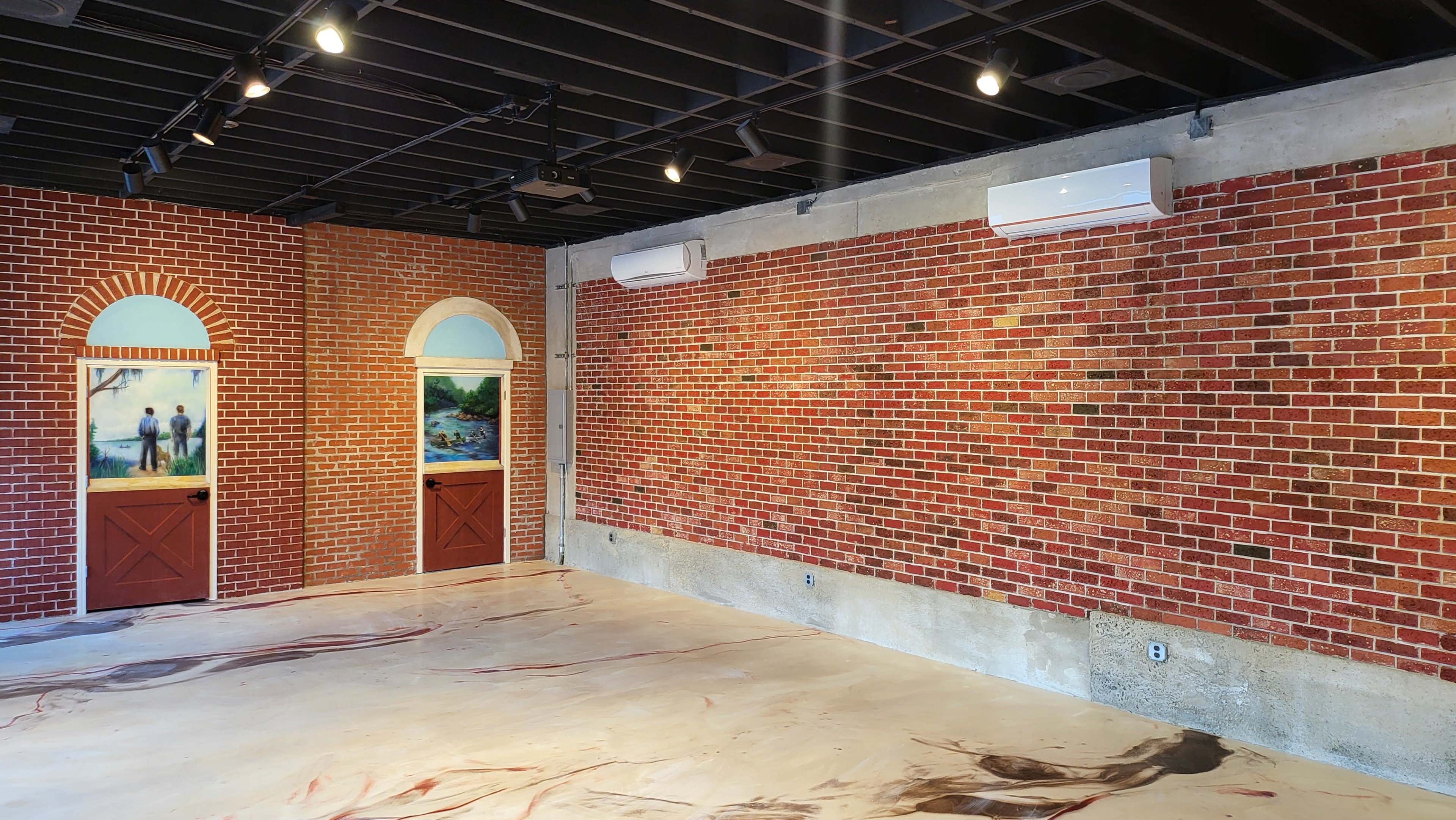 The image shows an interior space with exposed brick walls, two doors featuring artwork, and a smooth, marbled concrete floor.