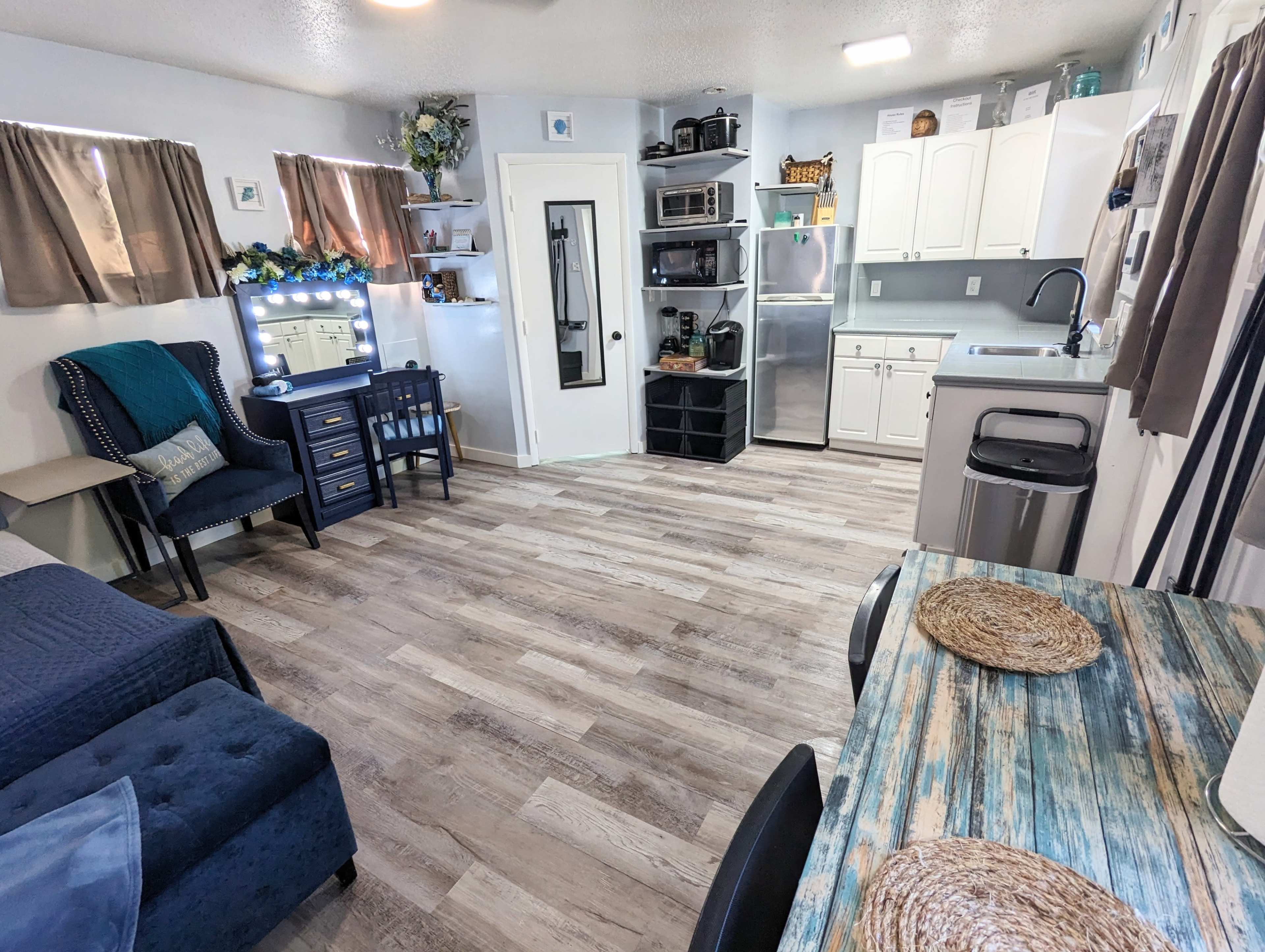 A small, modern kitchen and living area with a sofa, dining table, and various kitchen appliances.