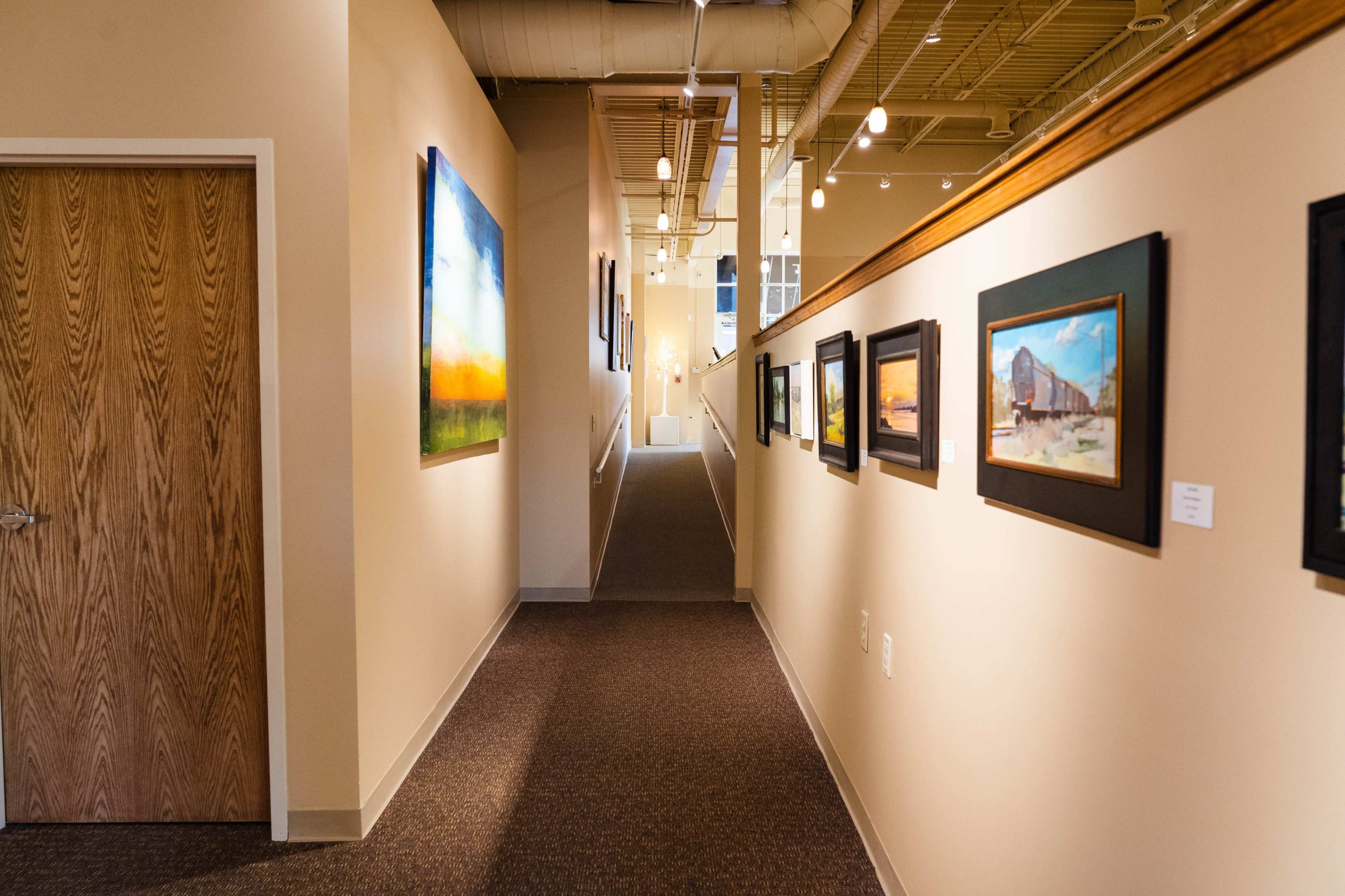 A well-lit corridor features framed artwork on the walls, leading to a staircase at the far end.